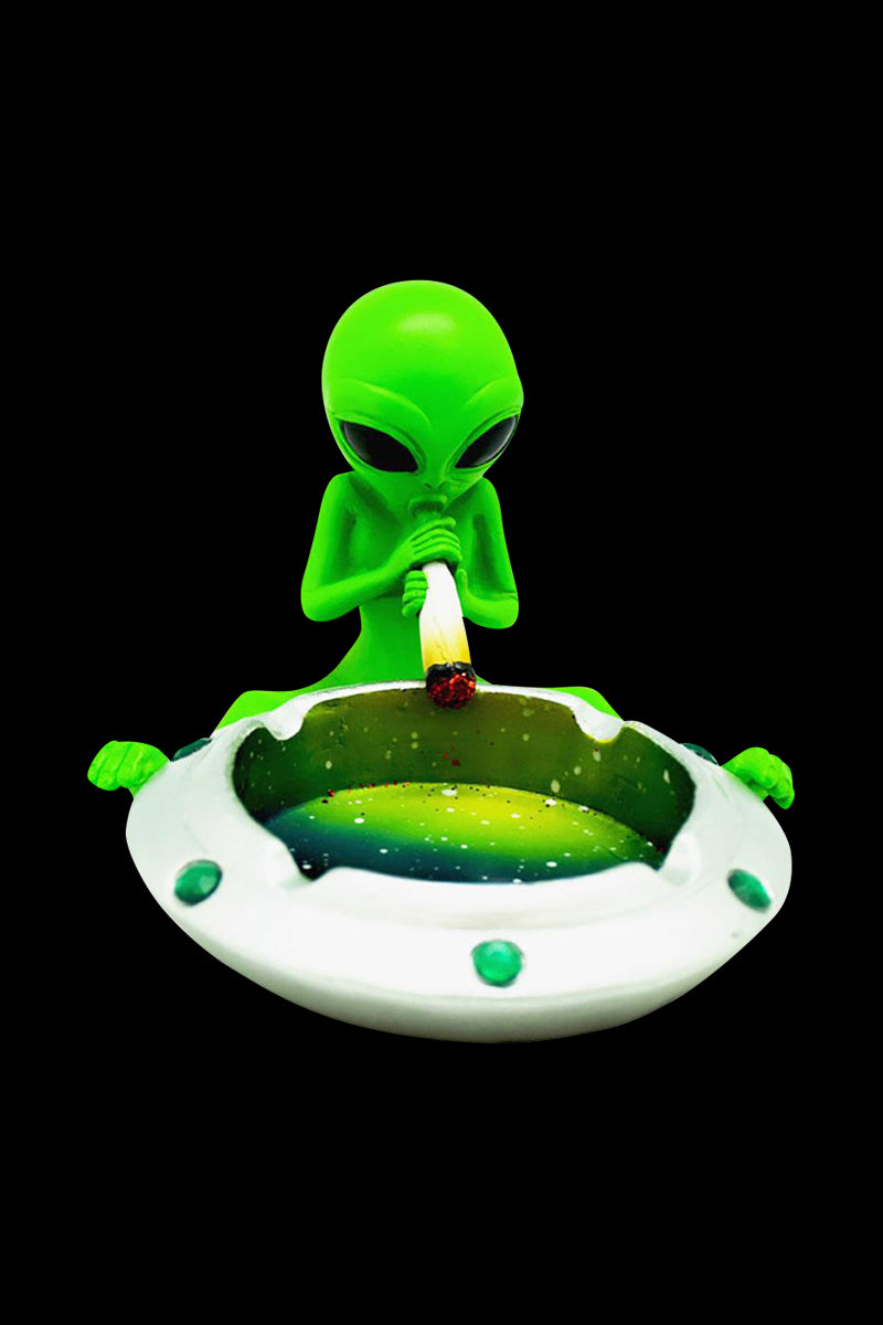 Centered front view of a bright green alien holding a lit joint above a white UFO ashtray in the Astral Alien Smoke Session Ashtray.