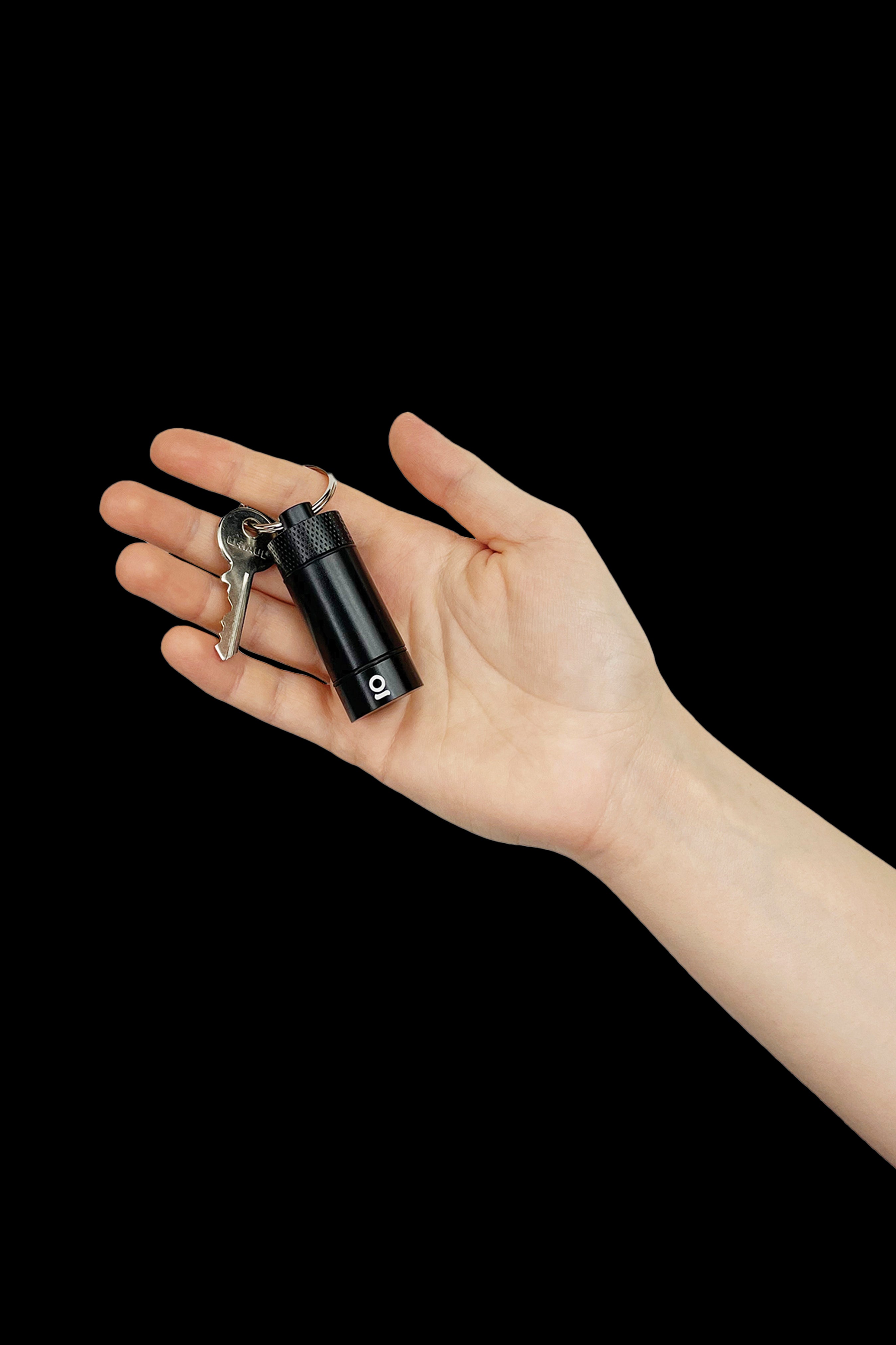 Hand holding a sleek, black cannabis oil vape pen with keys attached against a dark background.