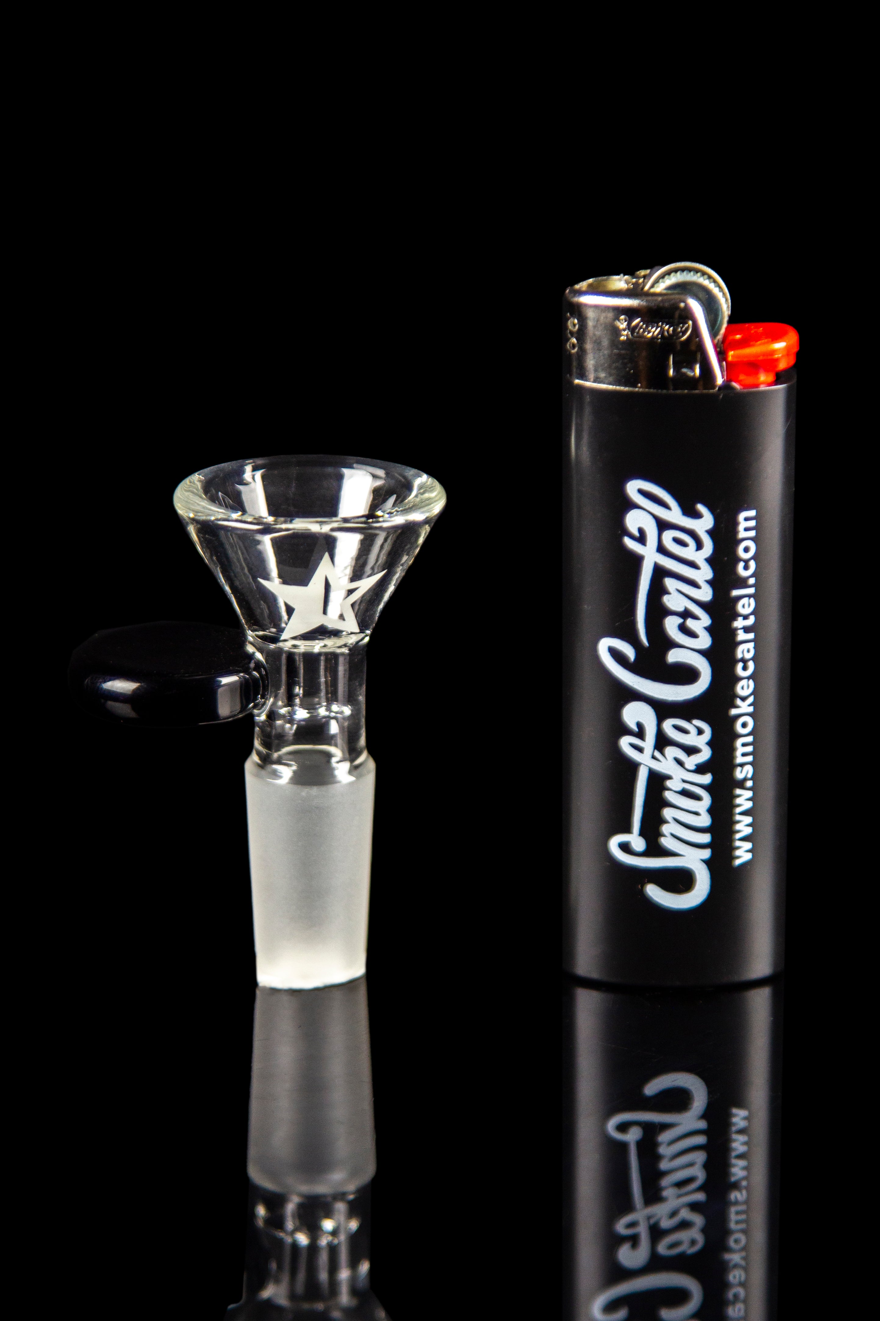 Close-up, side view of the Famous Brandz Glass Beaker Ice Bong - Space bowl piece with a white star decal beside a black lighter on a reflective black background