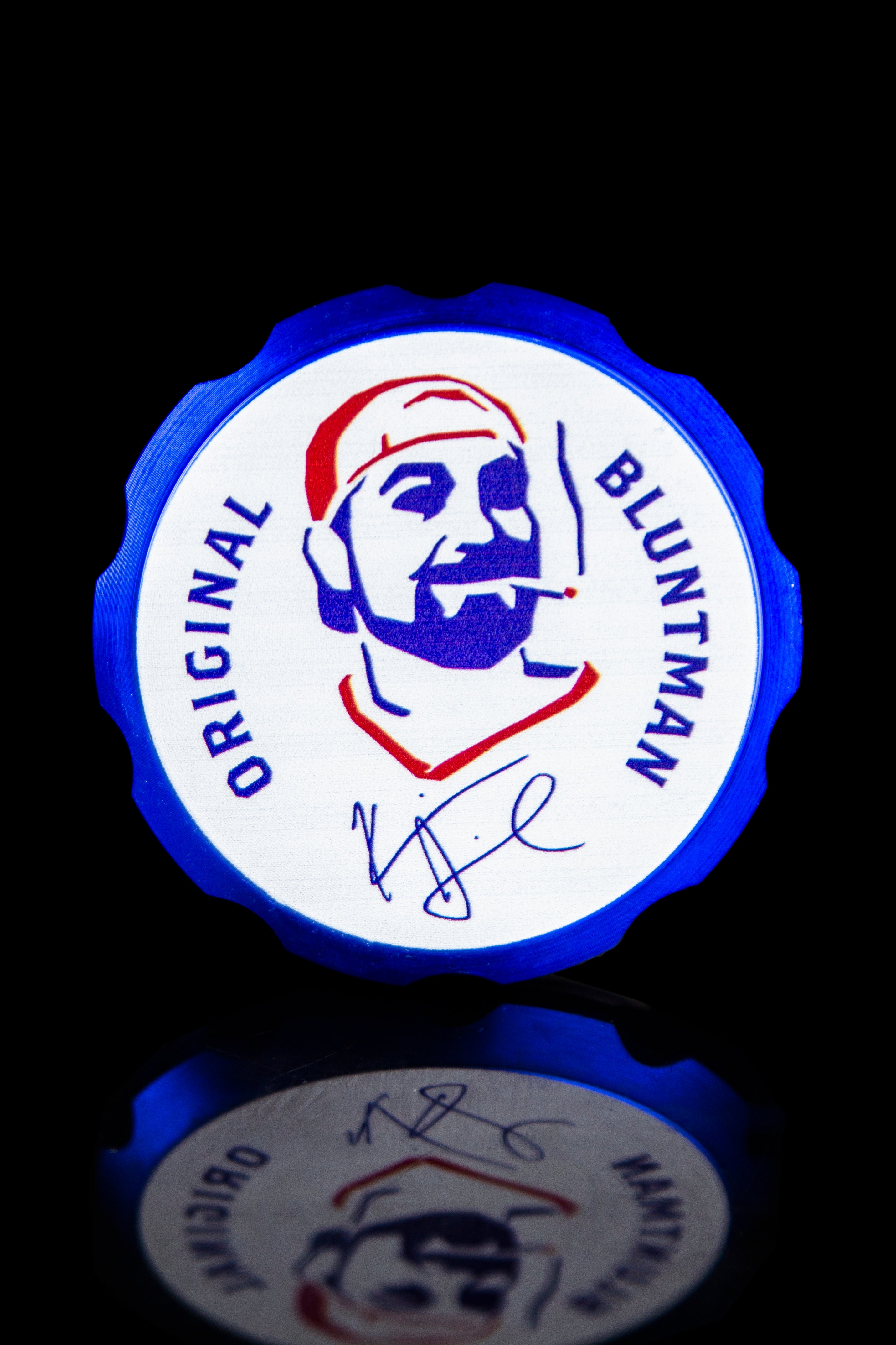A blue and white collectible poker chip featuring a cartoon portrait of a bearded man wearing a red hat, branded “Original Bluntman” with a signature below.