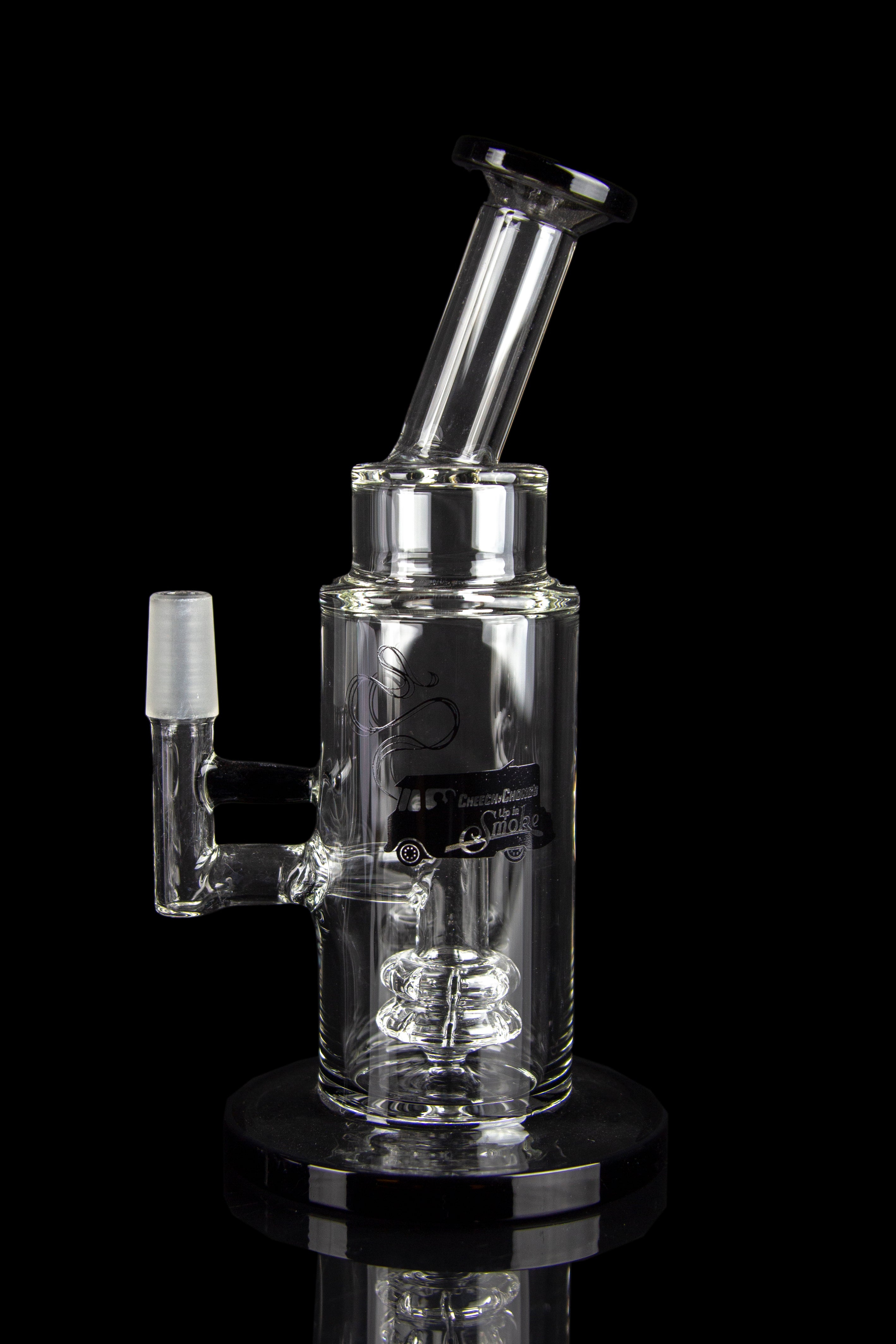 Clear glass water pipe (rig) with intricate bubbler design, reflecting on a glossy black surface.