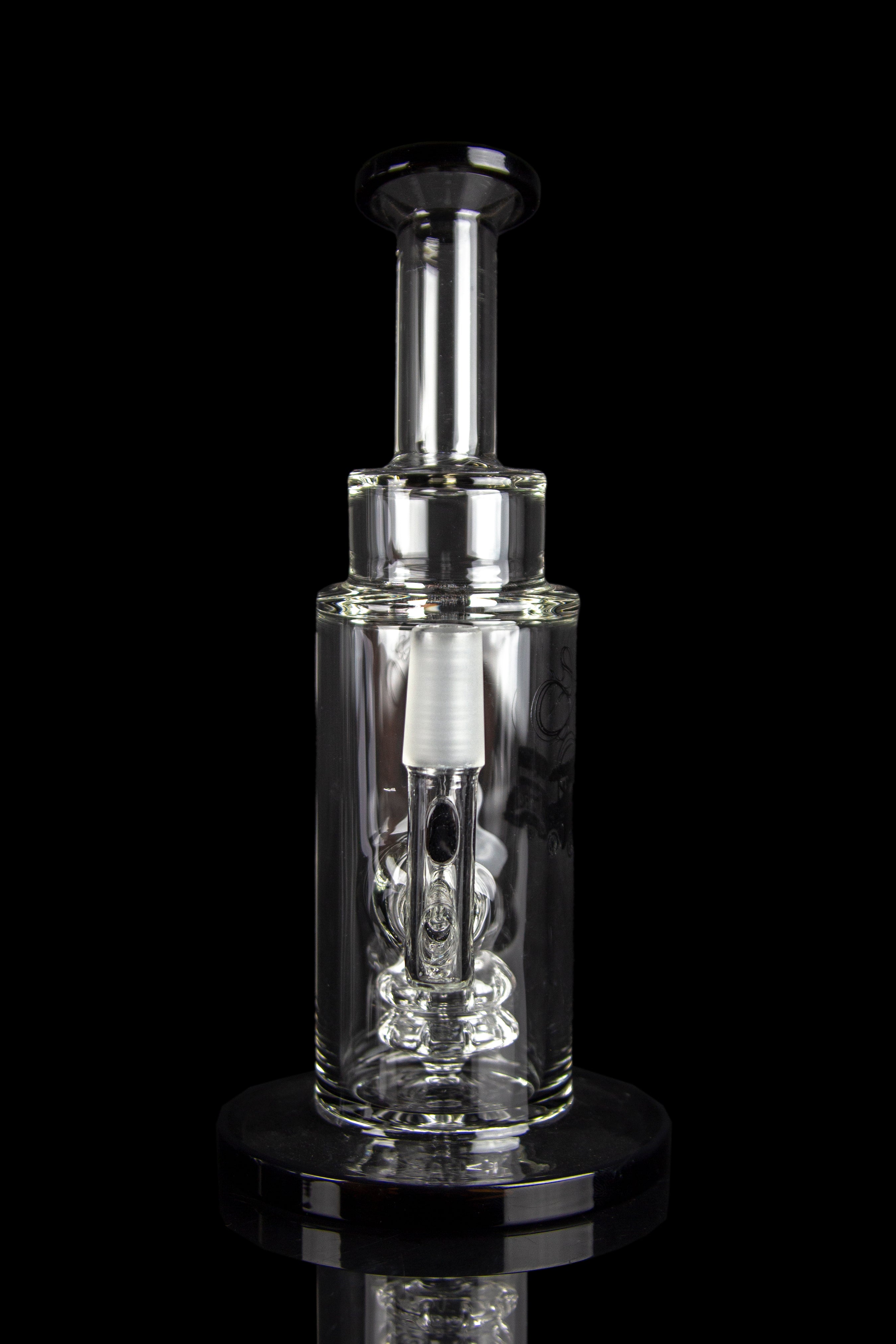 Clear glass oil rig with intricate bubbler design, displayed on a reflective surface against a black background.
