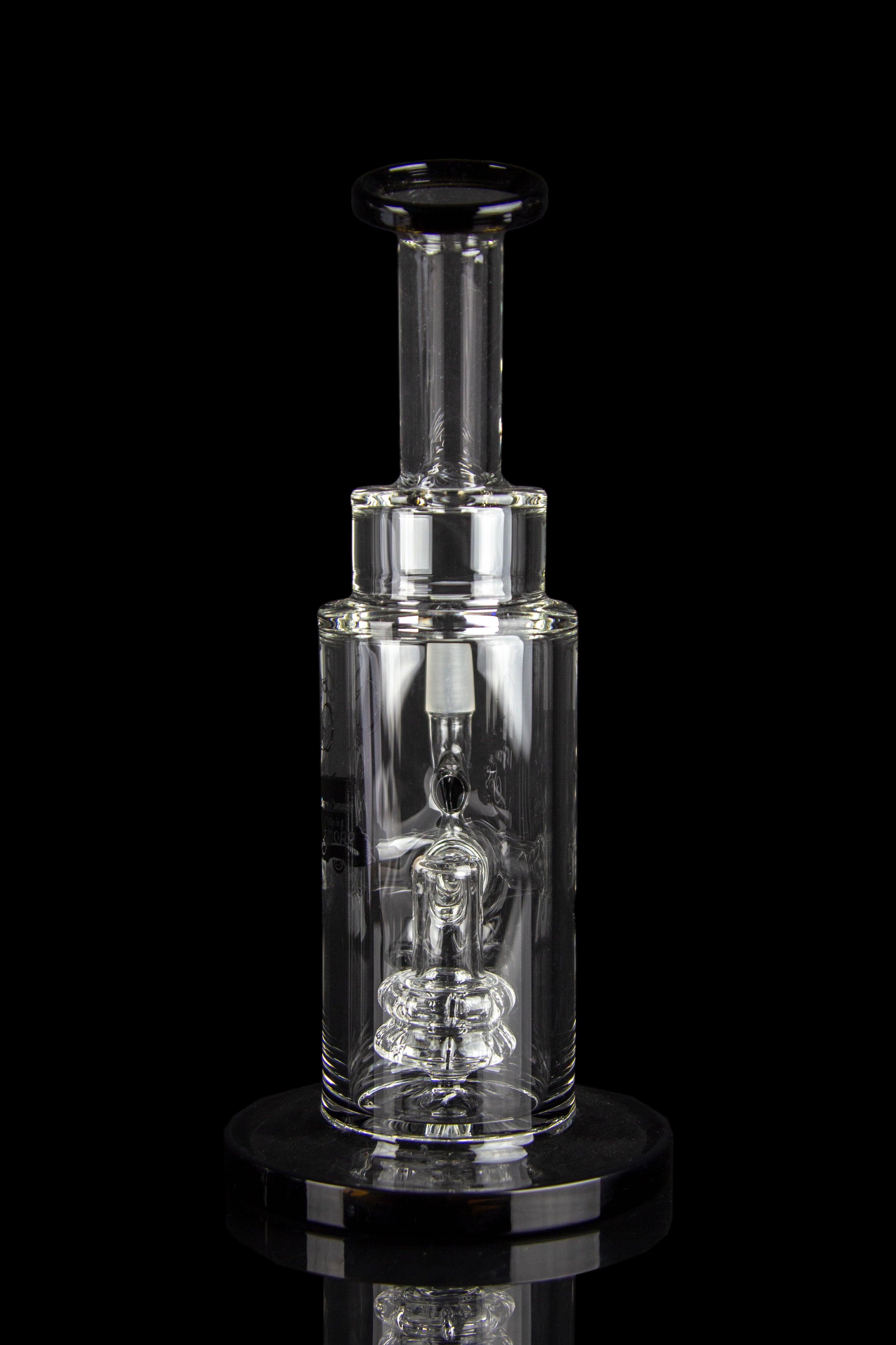 Clear glass dab rig with intricate percolator and vapor pathway, displayed on a reflective surface.