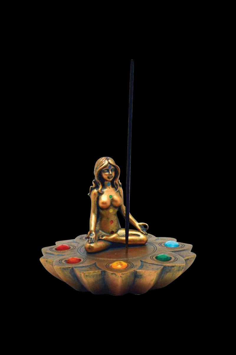 A side view of the Bronze Chakra Stones Incense Burner featuring a sculpted figure atop a circular stone base, illuminated by a lit incense stick.