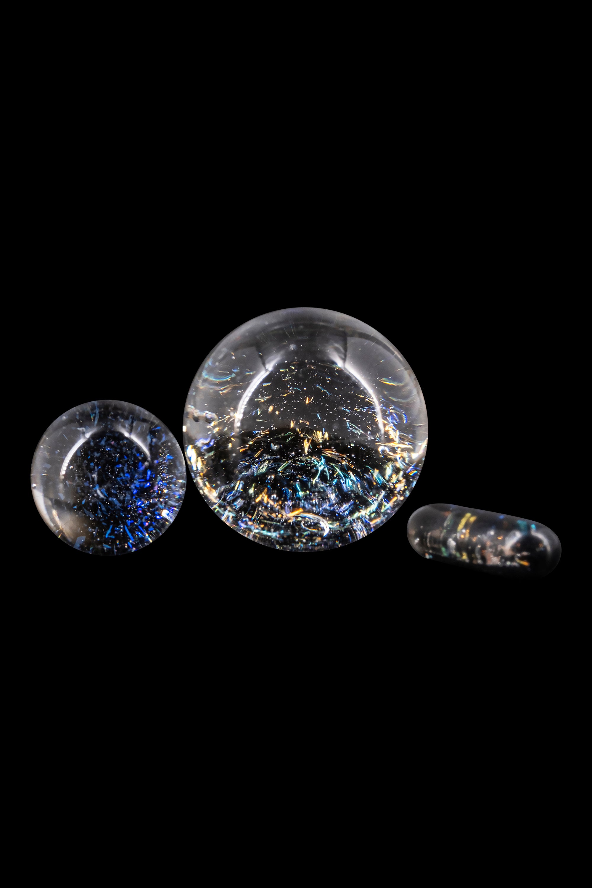 Glass marbles with colorful, speckled inclusions, likely for use with cannabis concentrates, displayed on a black background.