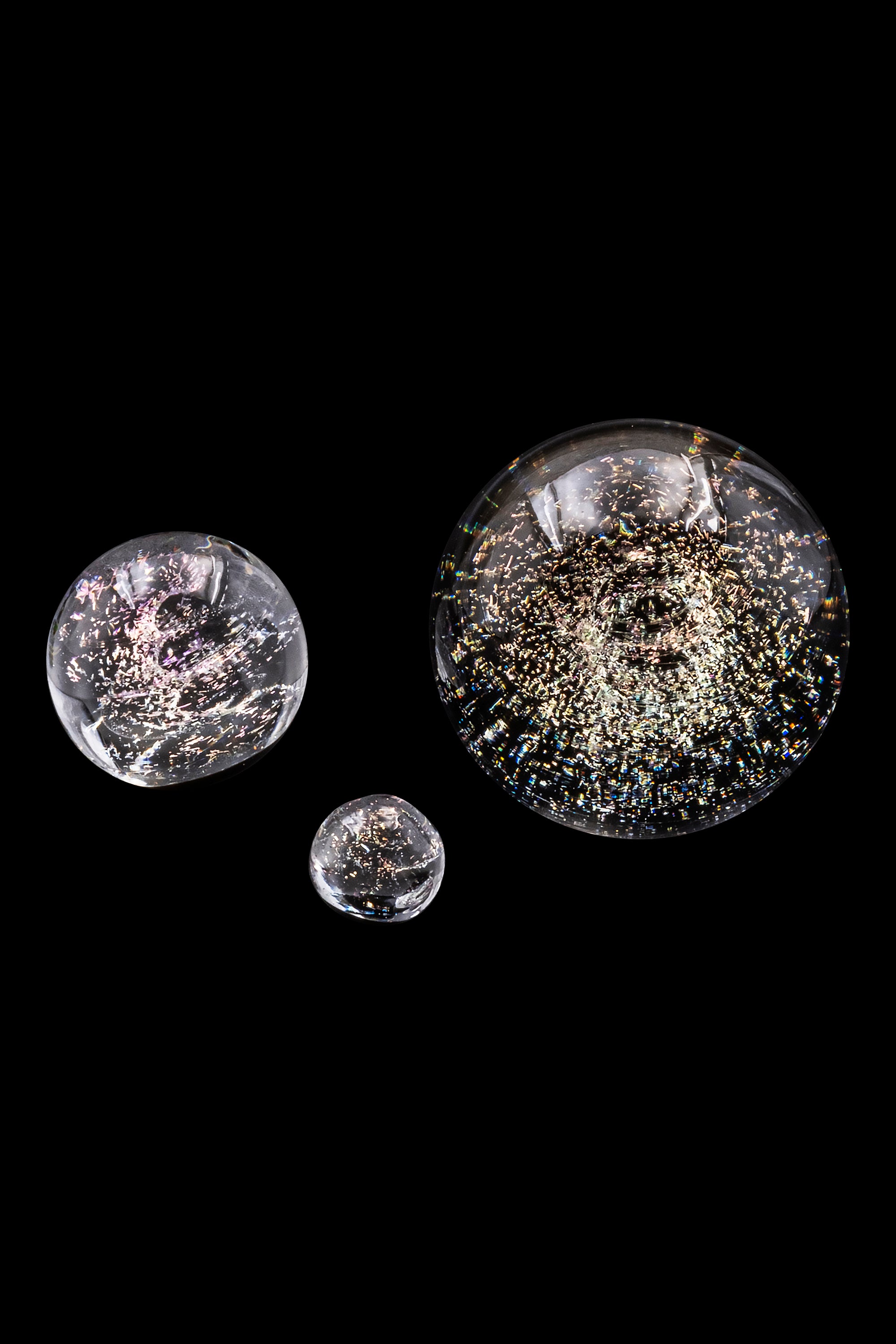 Close-up of three clear glass or acrylic bubbles filled with colorful cannabis flower fragments against a black background.