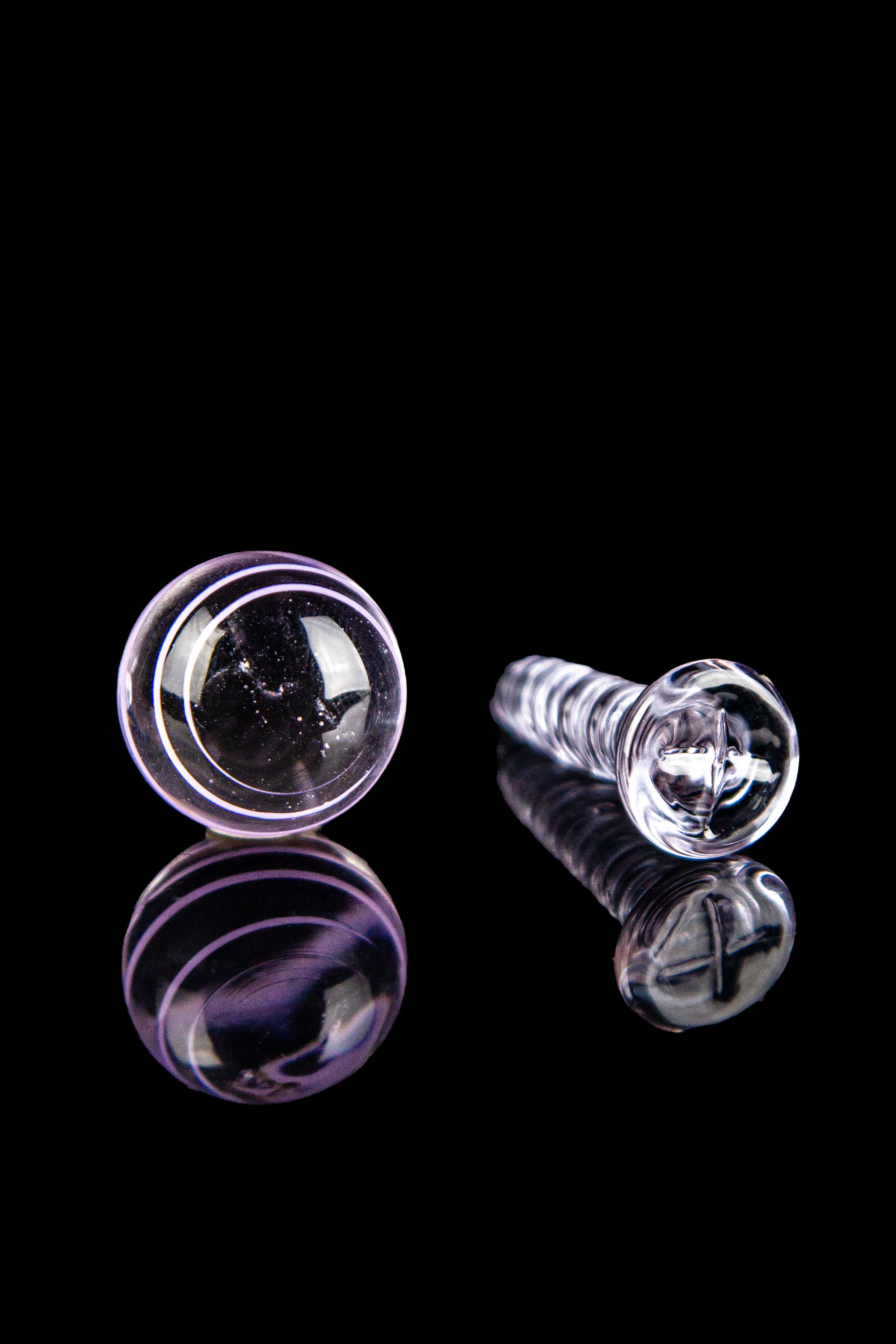 Purple and clear glass cannabis oil rig tips with reflections on a black background.