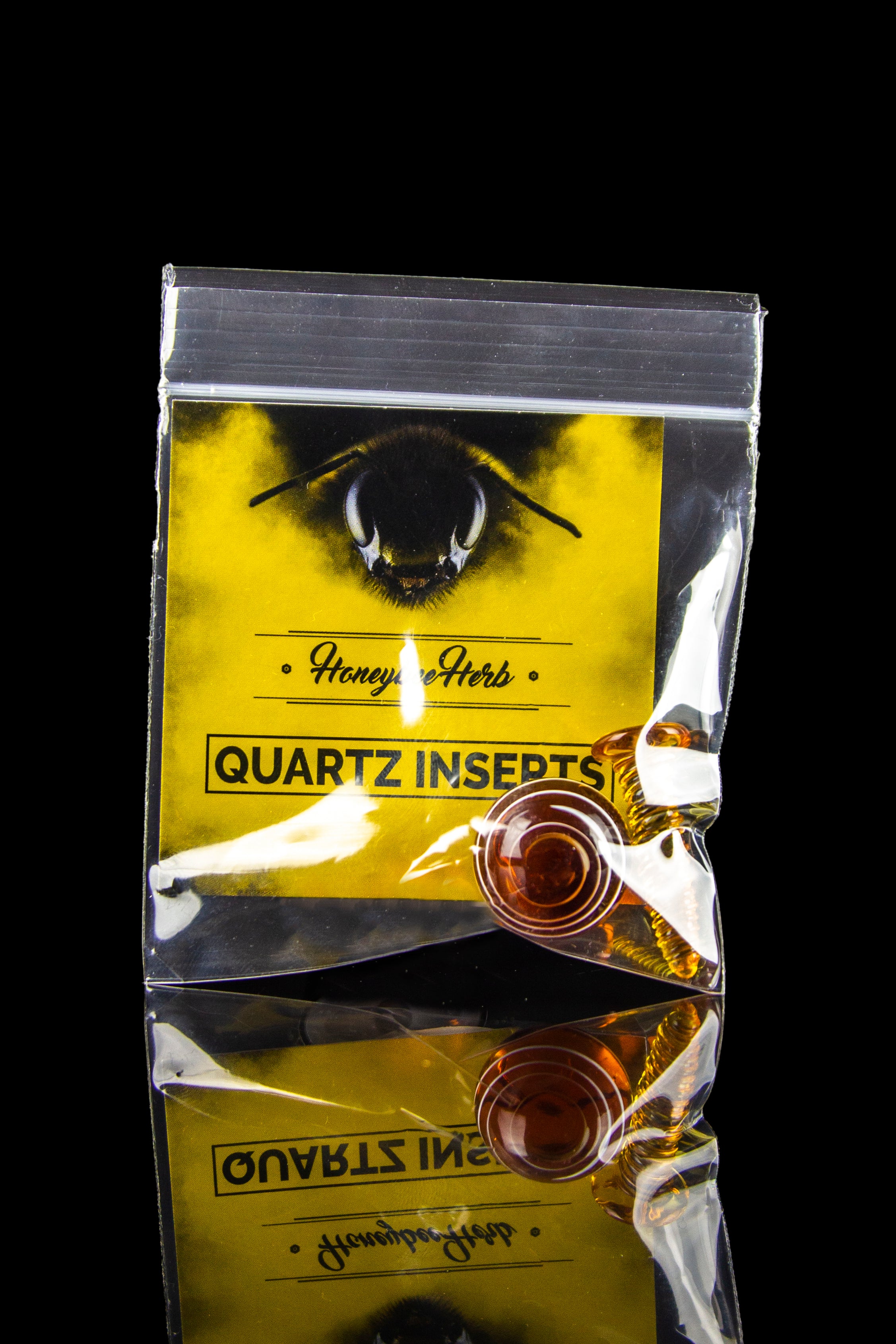 Yellow mylar bag labeled “Honey & Herbs Quartz Inserts” containing two clear quartz inserts for a dab rig, against a black background.