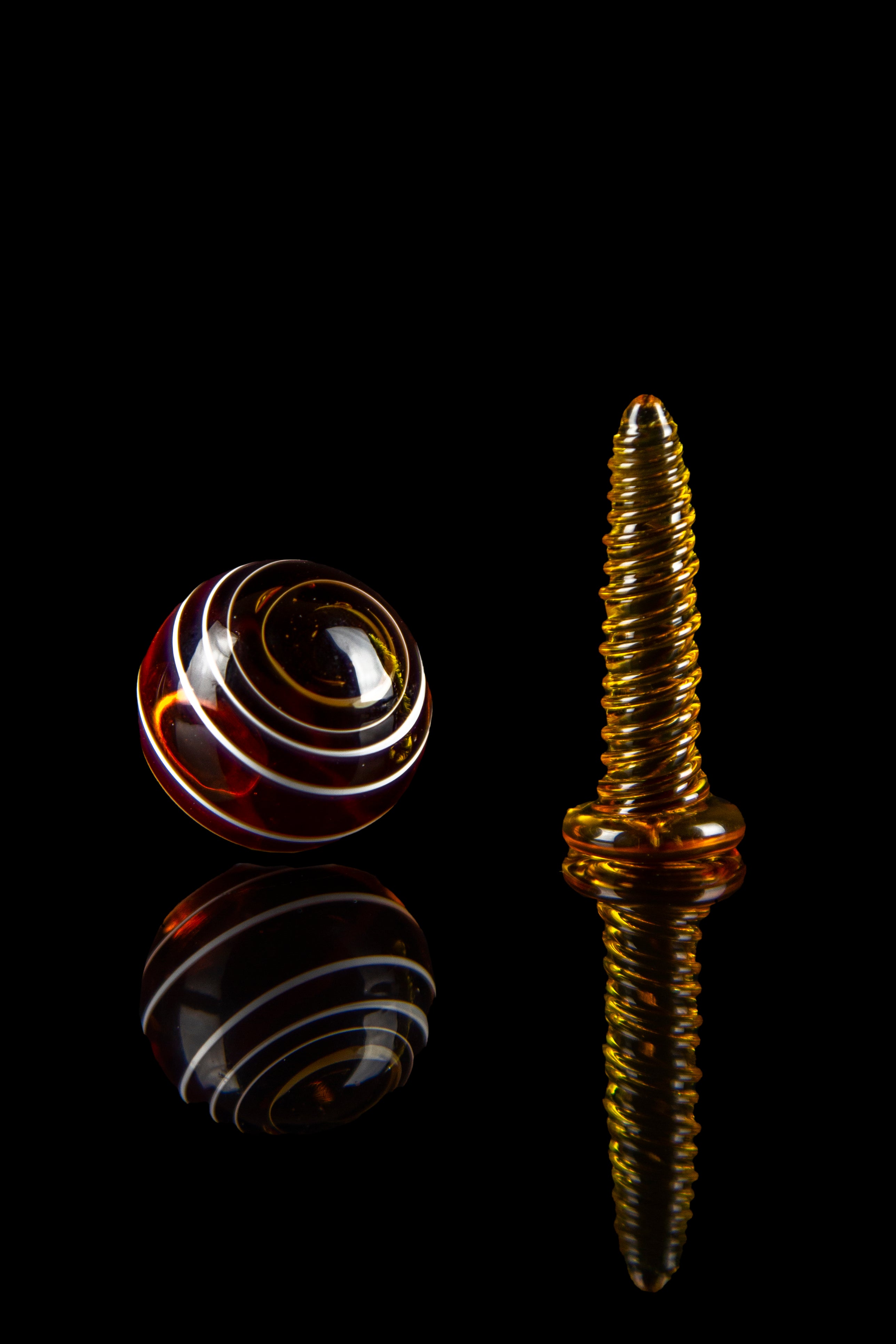 Amber glass cannabis oil burner and marble with reflections on a black background.