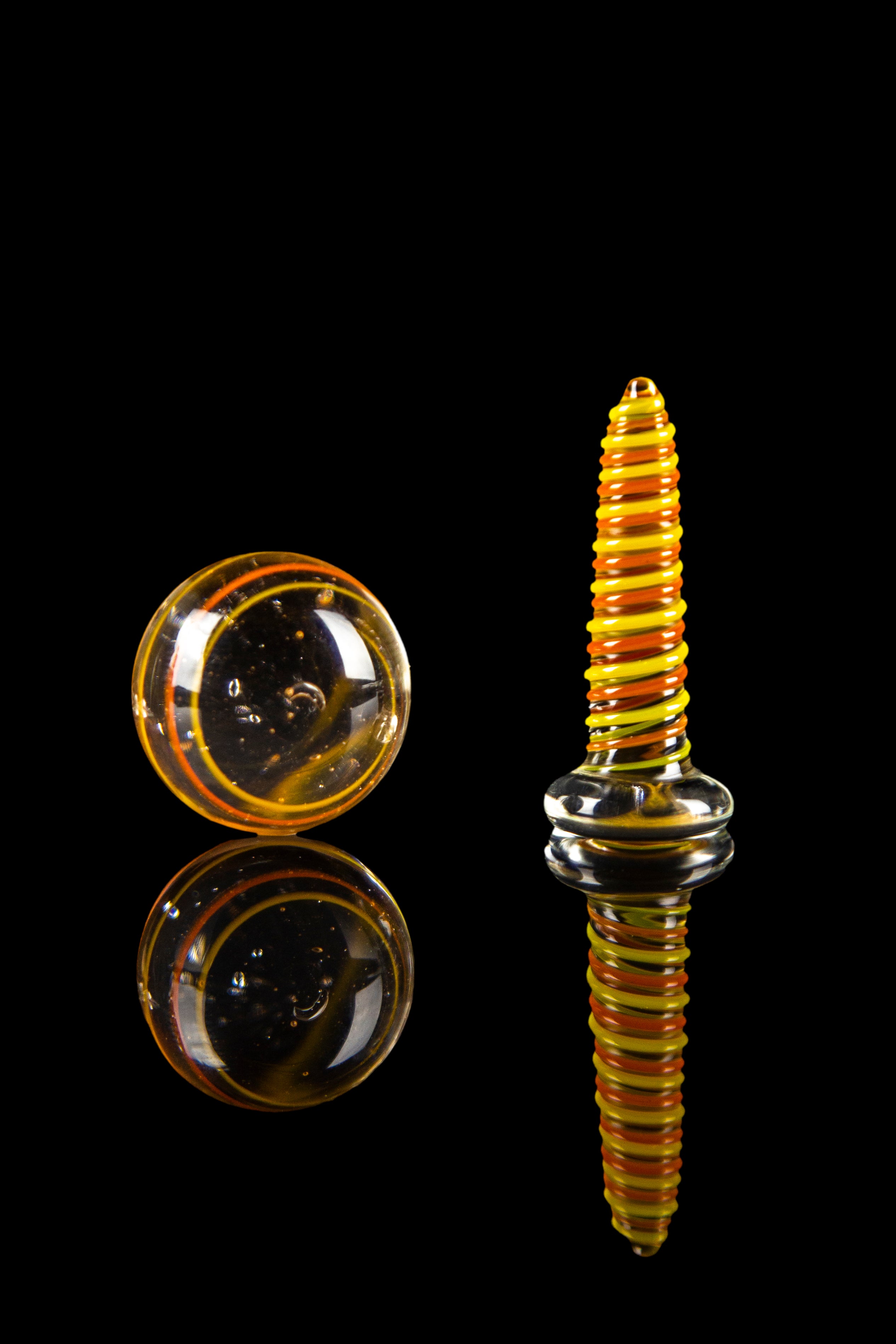 Hand-blown glass cannabis oil rig components, featuring a spherical marble and a spiral-patterned oil dome, displayed on a reflective black surface.