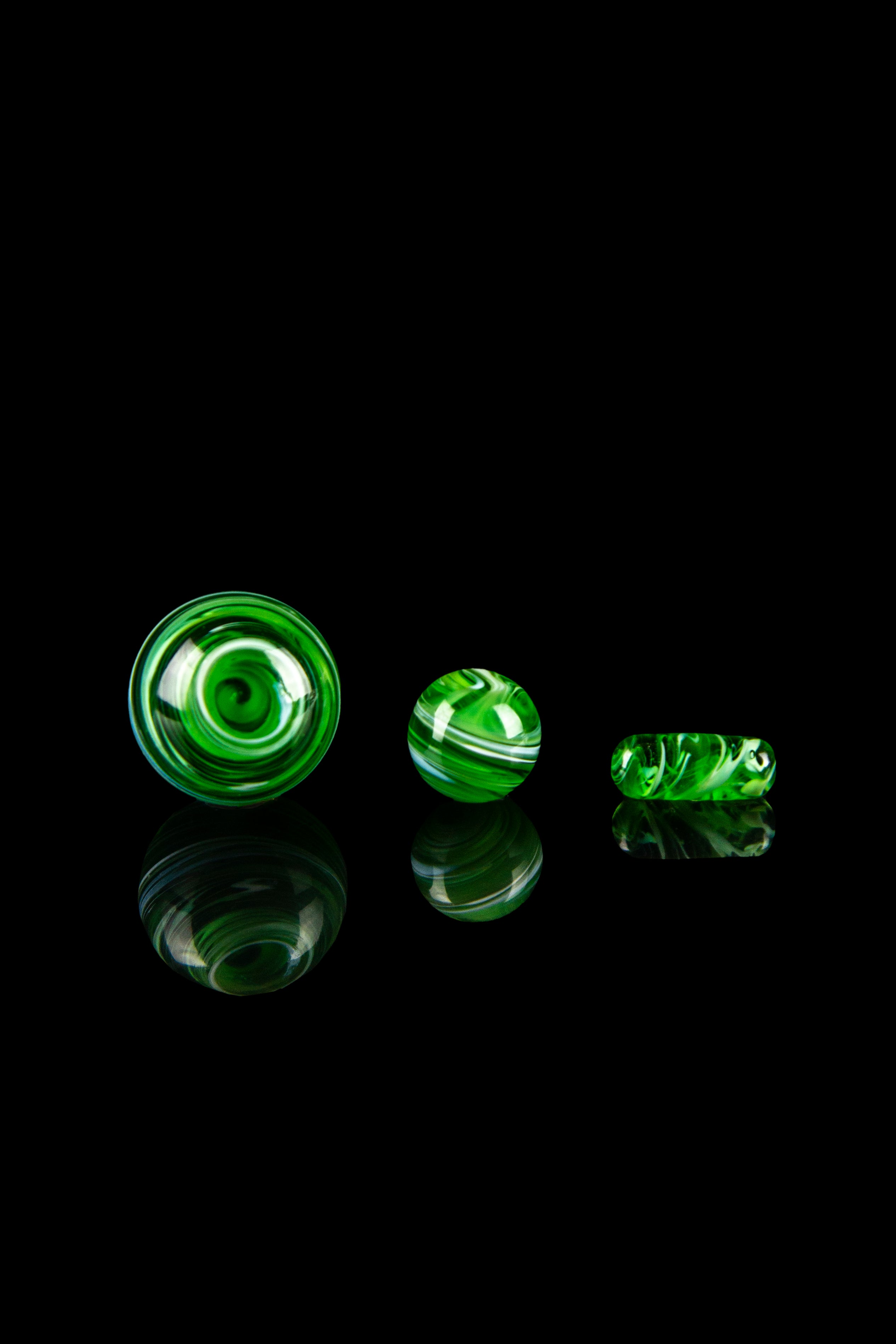 Green glass marbles with swirling patterns, reflecting on a black surface.