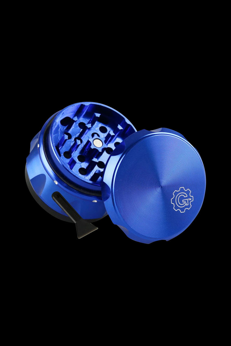 Angled close-up of the blue Pulsar Carver 4-Piece Grinder showing the open toothed chamber, magnet, and textured lid against a black background.