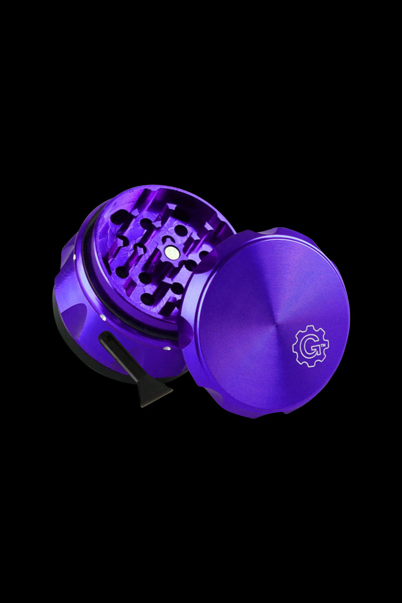 Angled close-up of the purple Pulsar Carver 4-Piece Grinder showing its open tooth-lined chamber, lid, and small scraping tool.