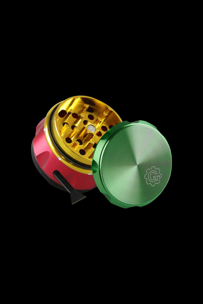 Angled close-up of the Rasta-colored Pulsar Carver 4-Piece Grinder showing its gold interior grinding teeth and green lid on a black background