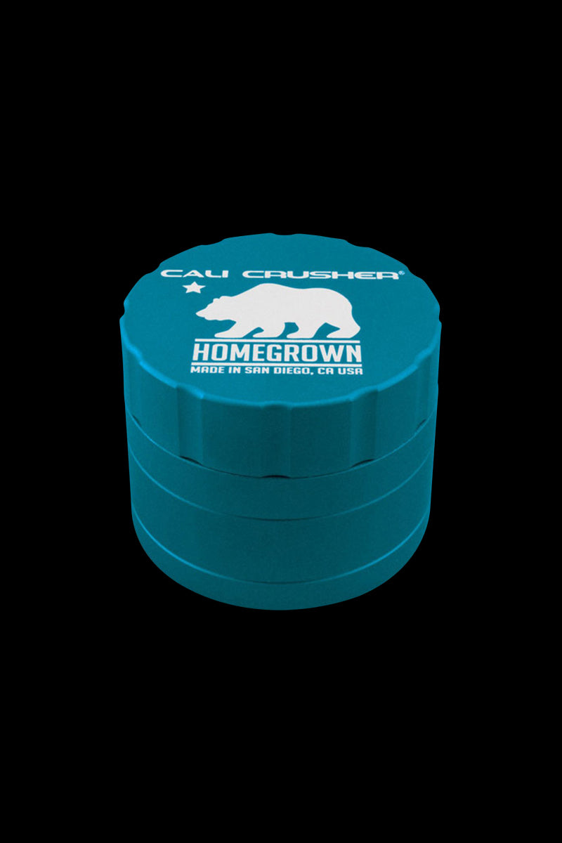Angled top-down view of a teal Cali Crusher Homegrown 4 Piece Grinder with white bear logo and stacked ridged sections against a black background