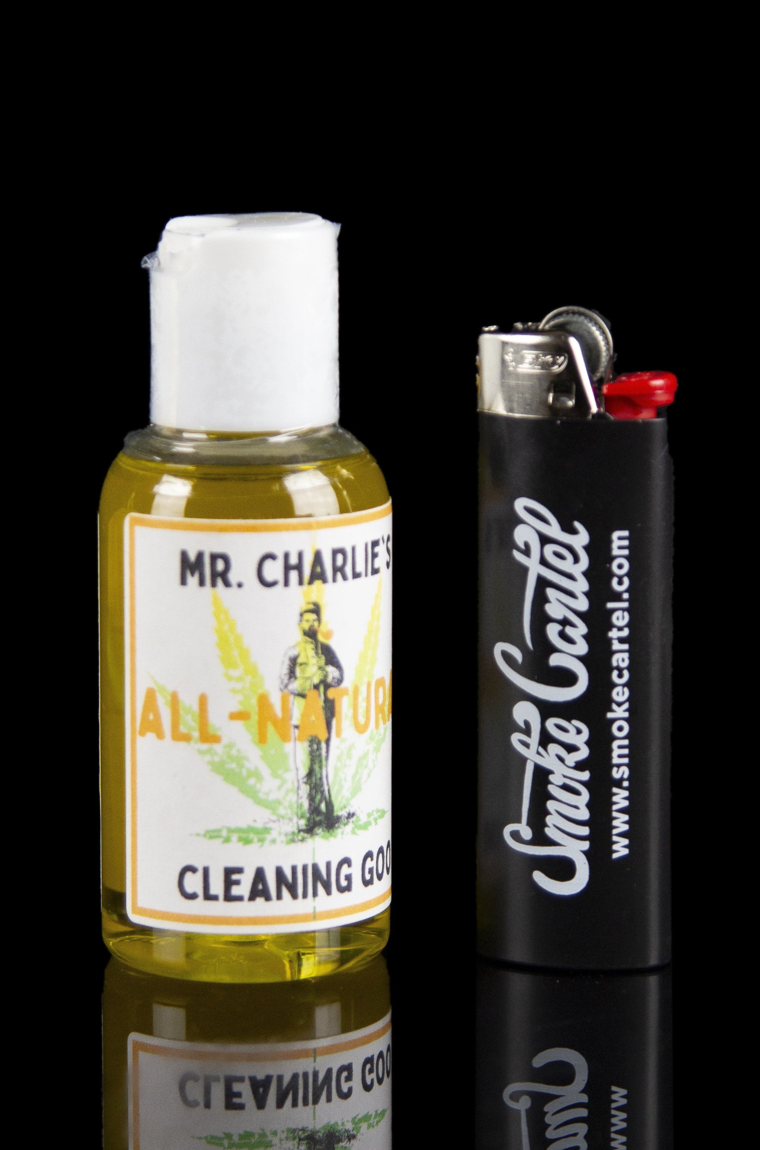 Bottle of cannabis cleaning solution and a lighter with "Smoke Cartel" branding, displayed on a reflective surface.