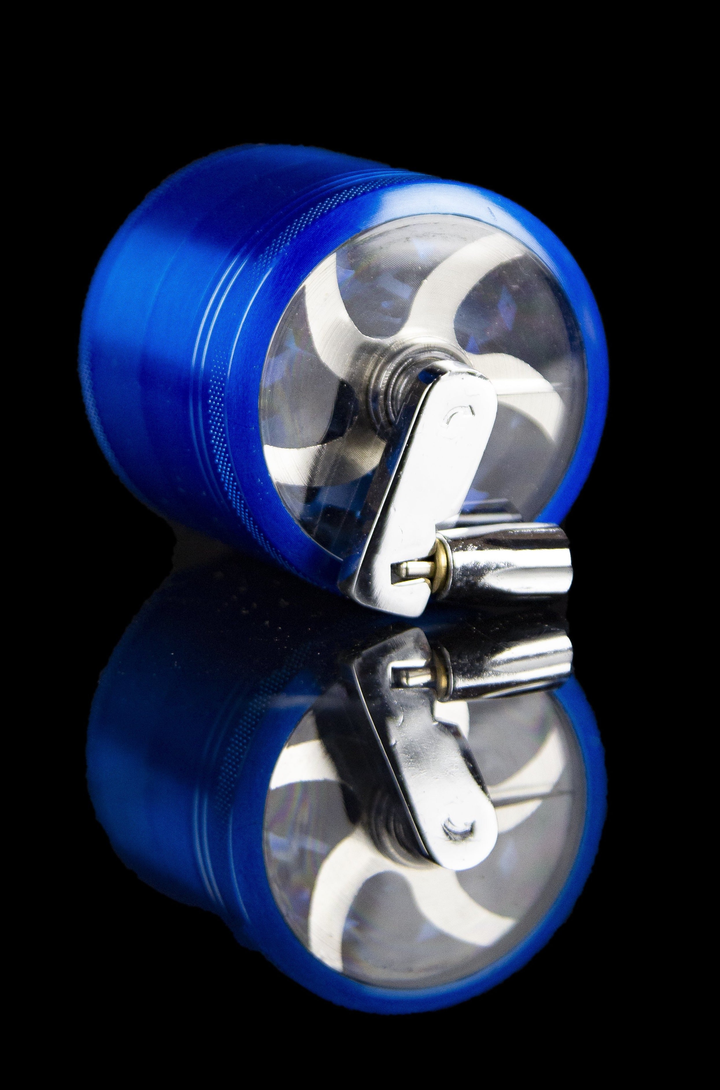 Blue cannabis grinder with transparent chamber and metal teeth, reflecting on a glossy surface.