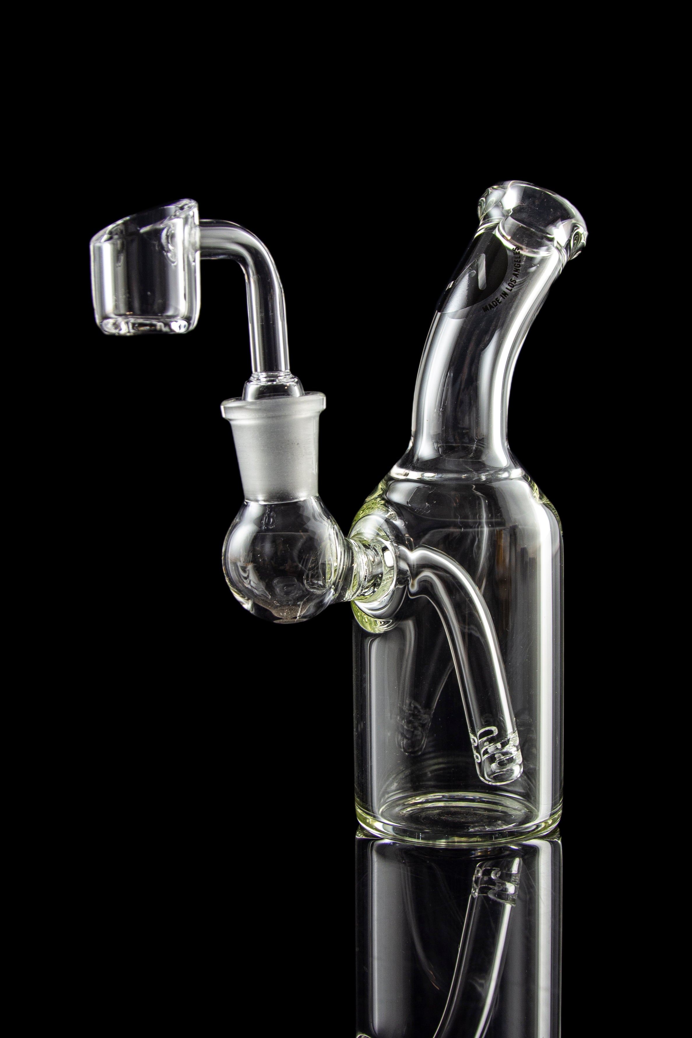 Clear glass dab rig with quartz banger, reflecting on a dark surface.