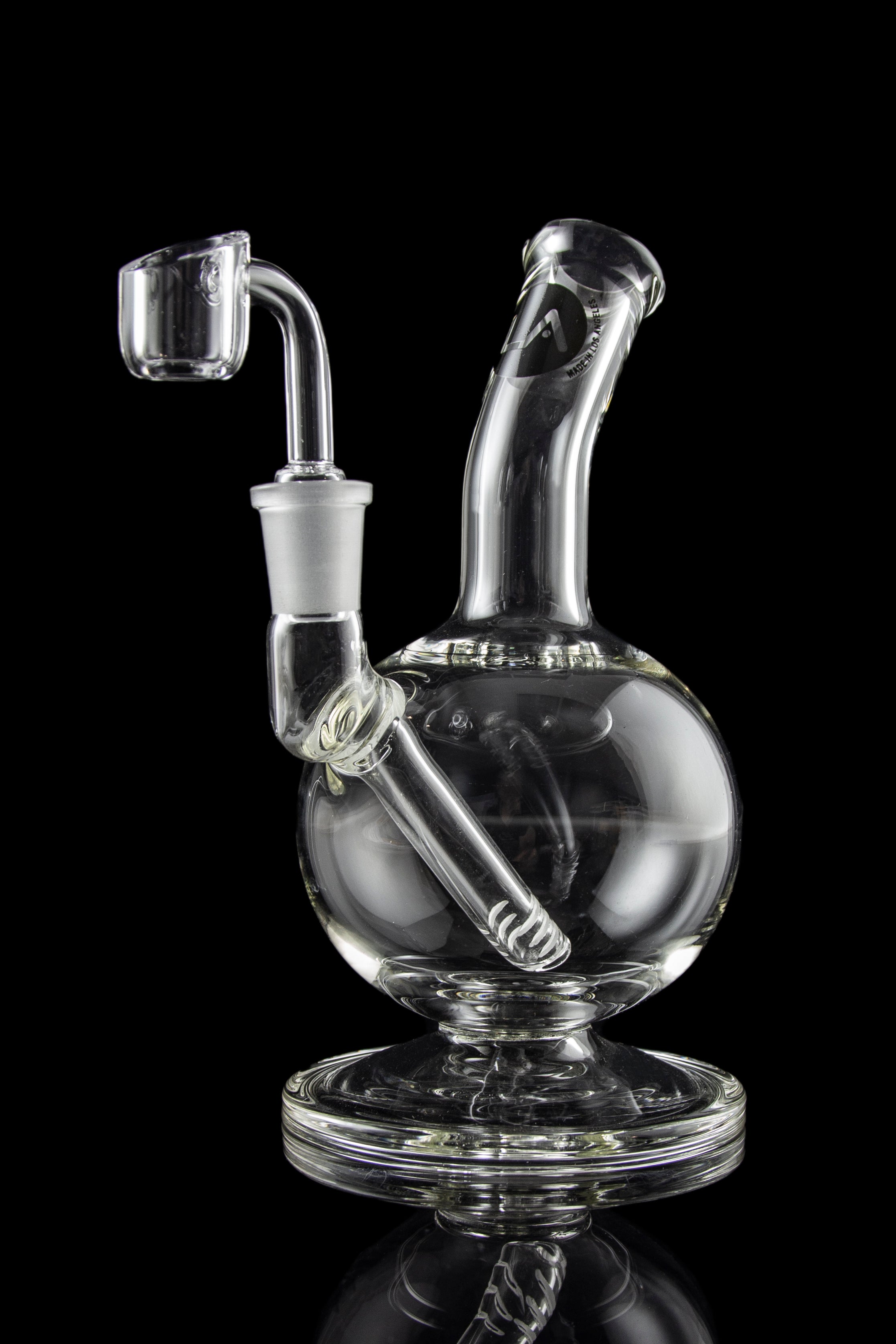 Clear glass dab rig with intricate design and accompanying nail, isolated on a black background.
