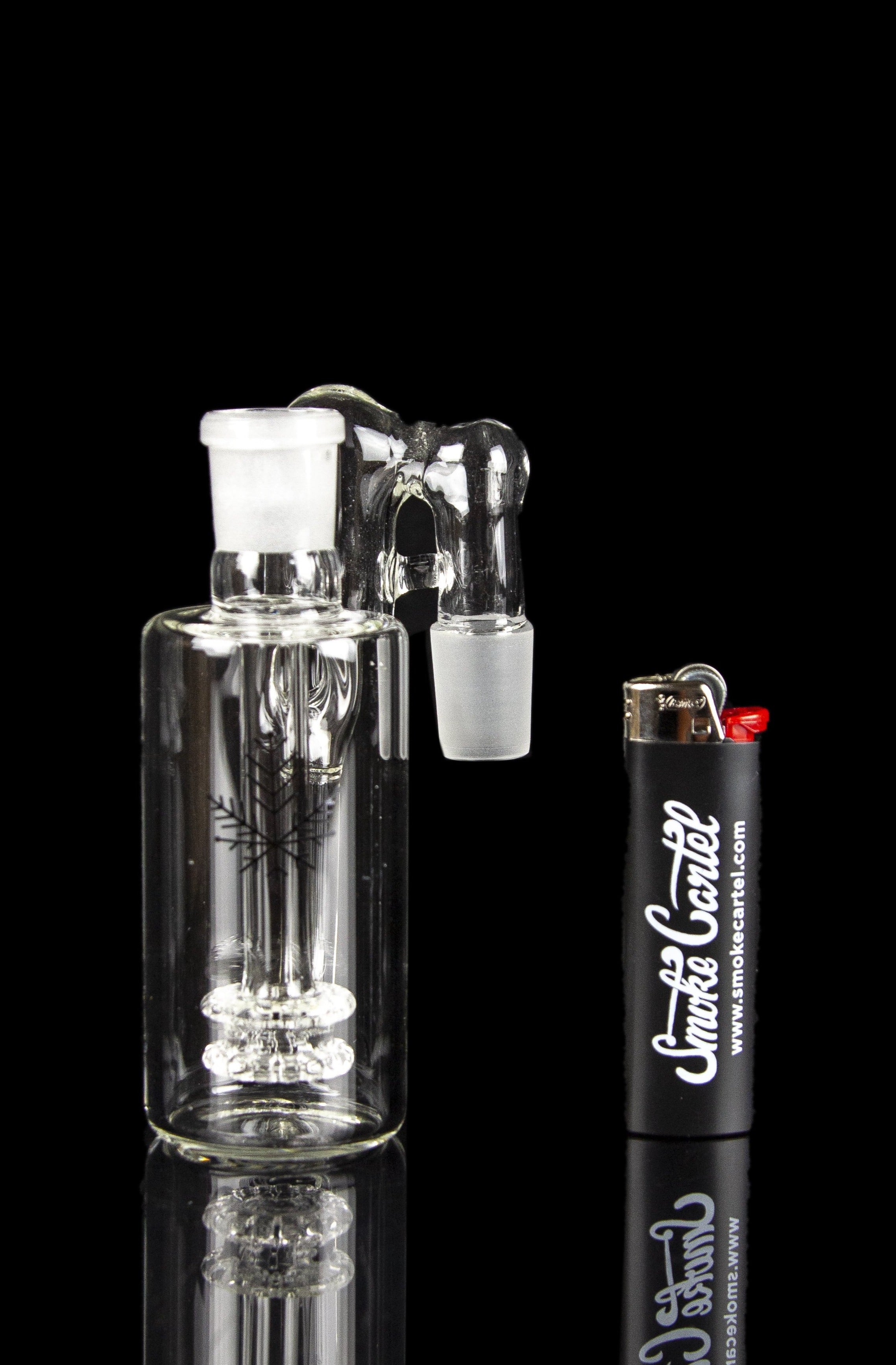 Glass bubbler with intricate design, reflecting on a black surface alongside a lighter branded with "Smoke Cartel".