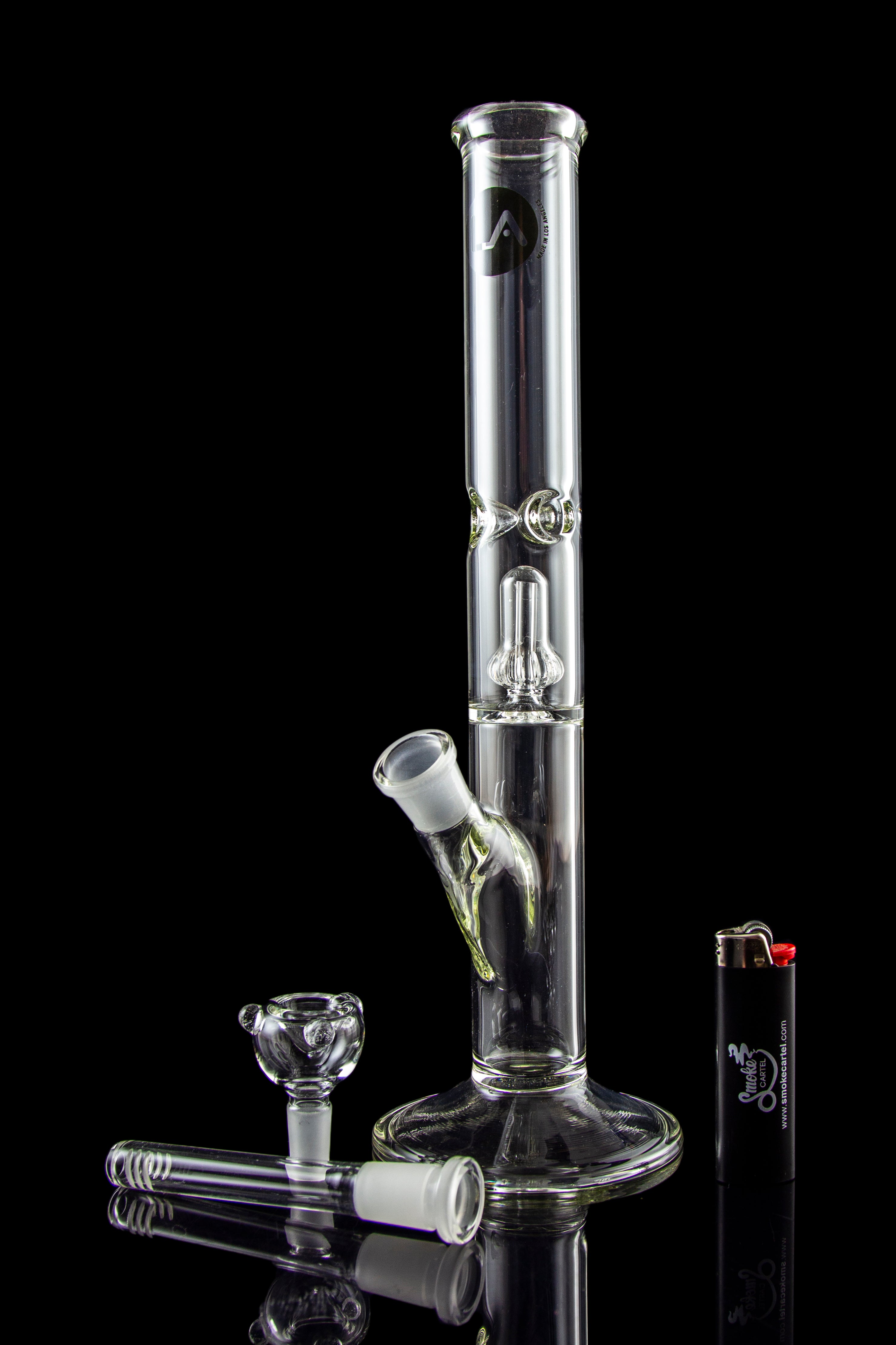 Glass bong with accessories on a reflective surface.