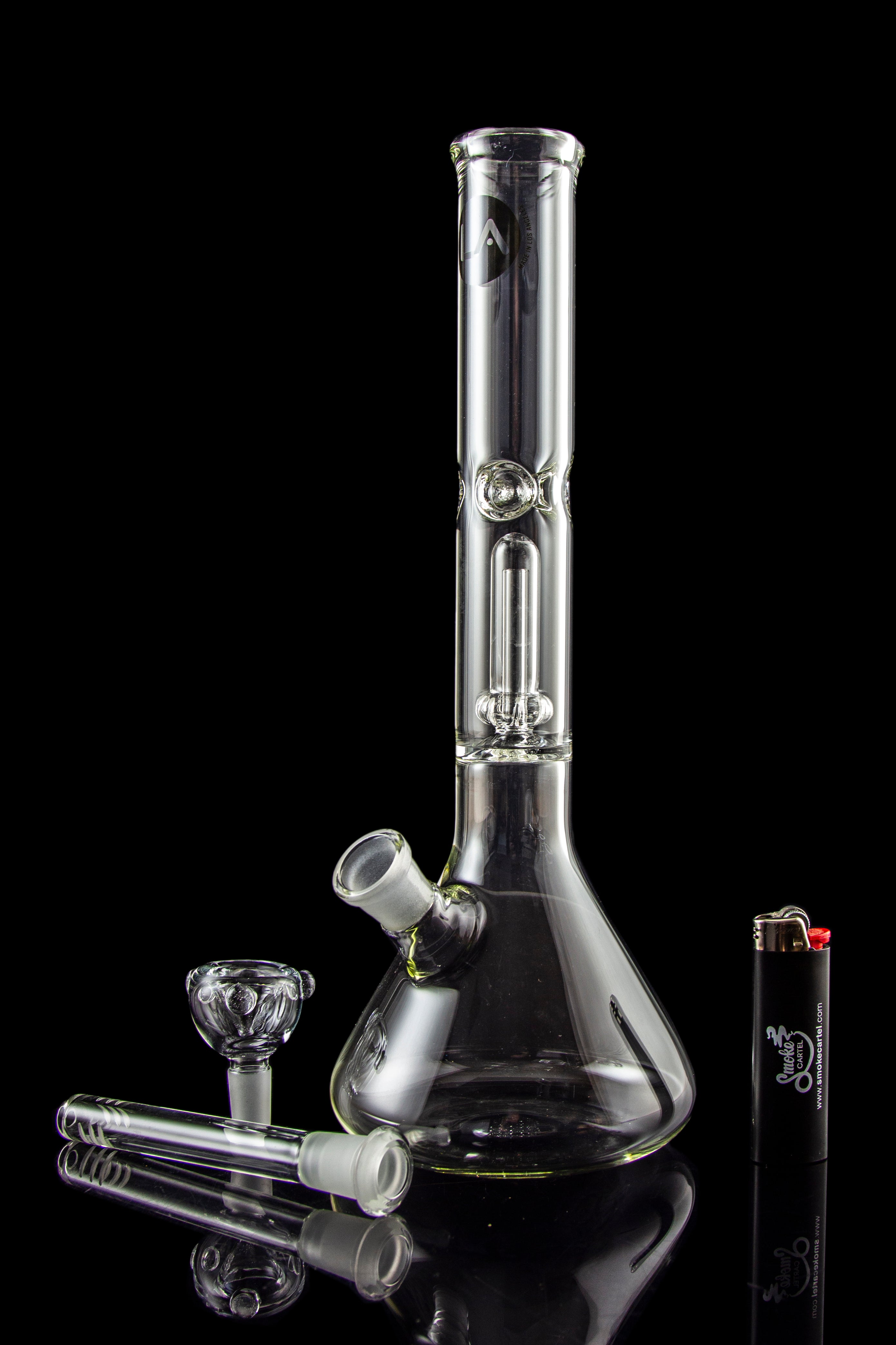 Glass bong with accessories and lighter on a reflective surface.