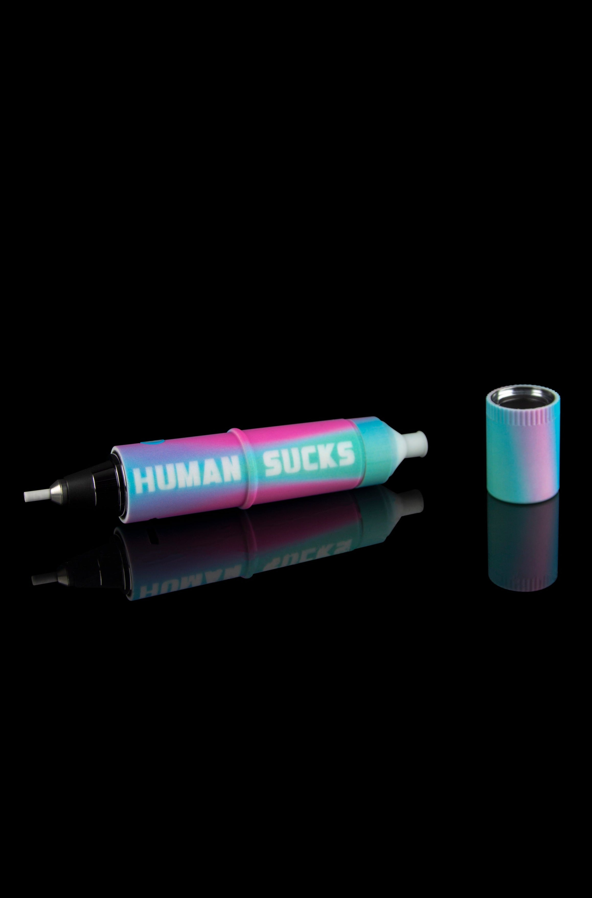 Iridescent cannabis oil syringe and accompanying mouthpiece reflected on a black surface, text reads "HUMAN SUCKS."