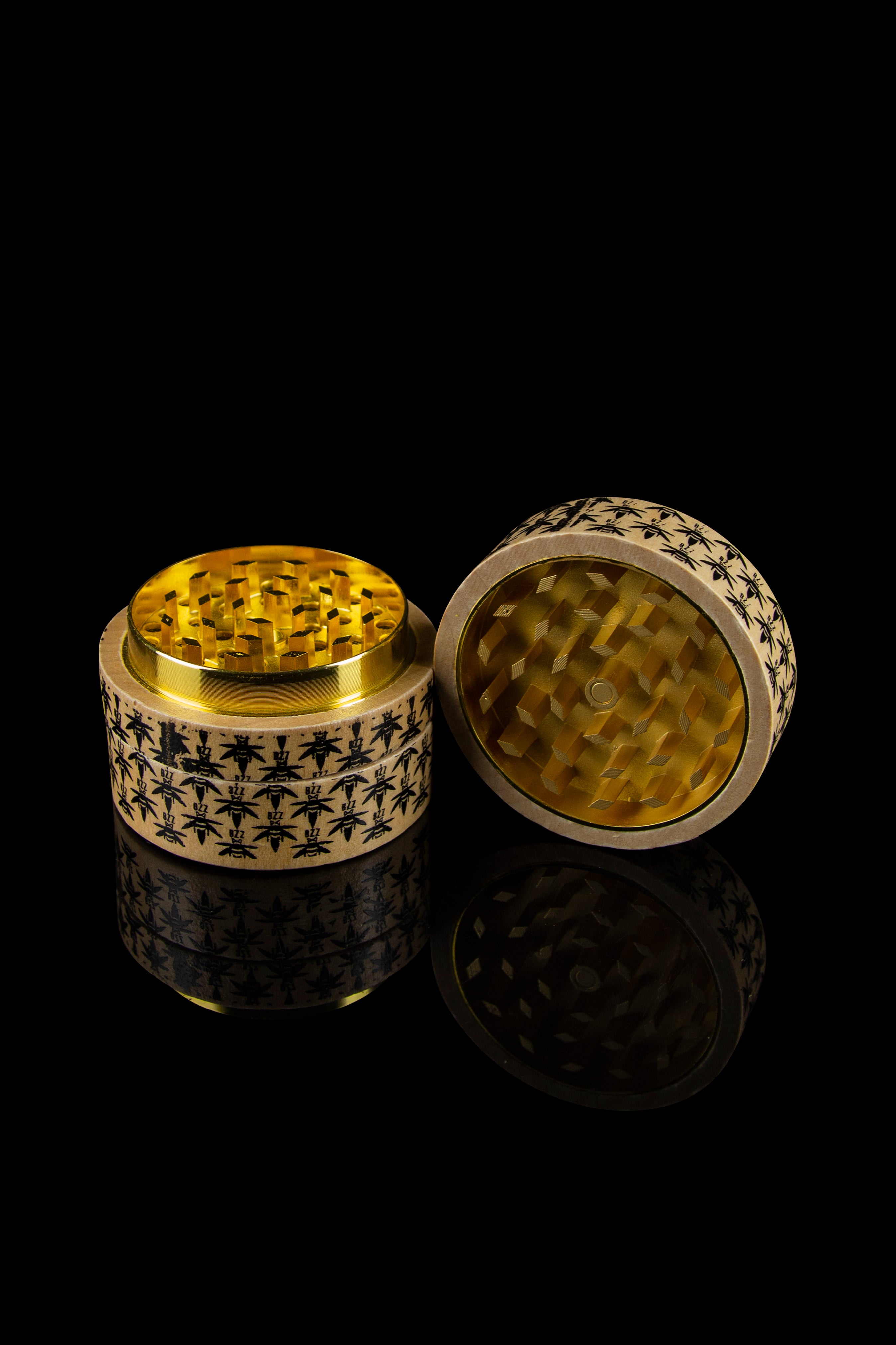 Gold cannabis grinder with intricate black geometric pattern, open to reveal the grinding mechanism, against a black reflective surface.