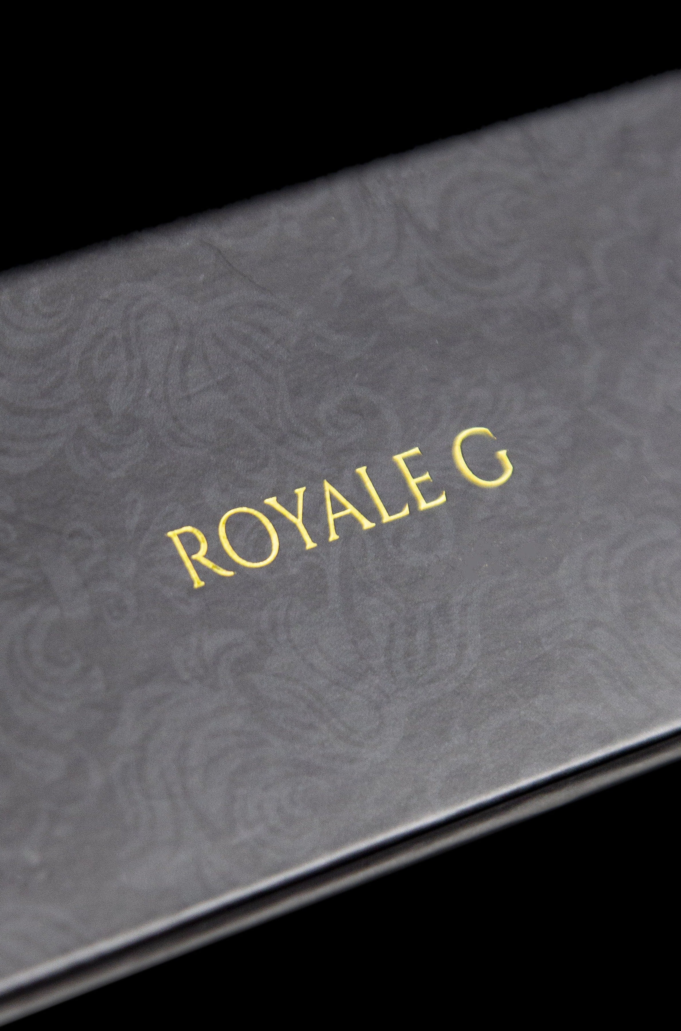 Close-up of a black box with gold foil lettering that reads "ROYALE G", suggesting luxury cannabis packaging.