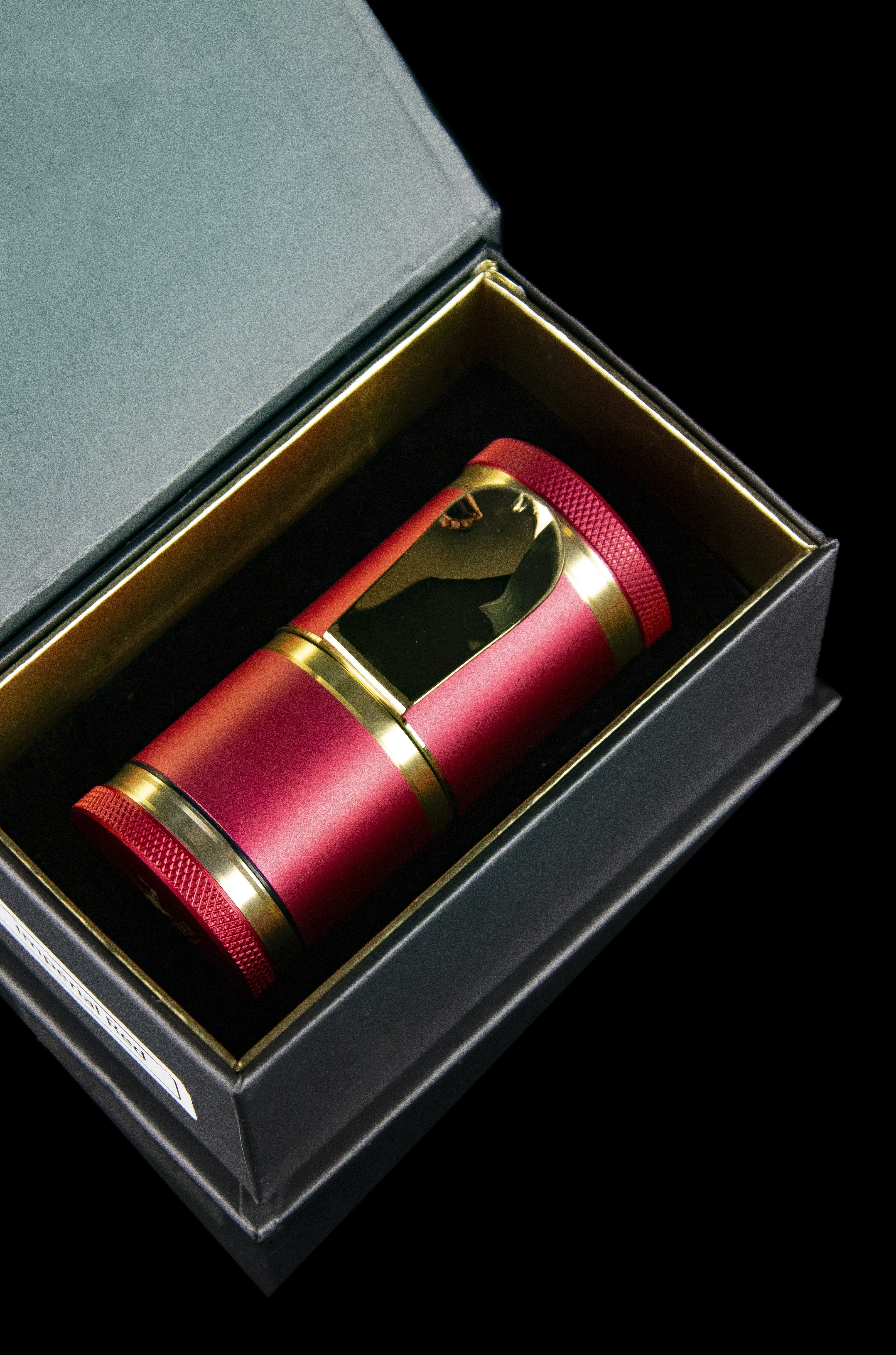 A luxurious red and gold cannabis grinder presented in a black box with gold interior.