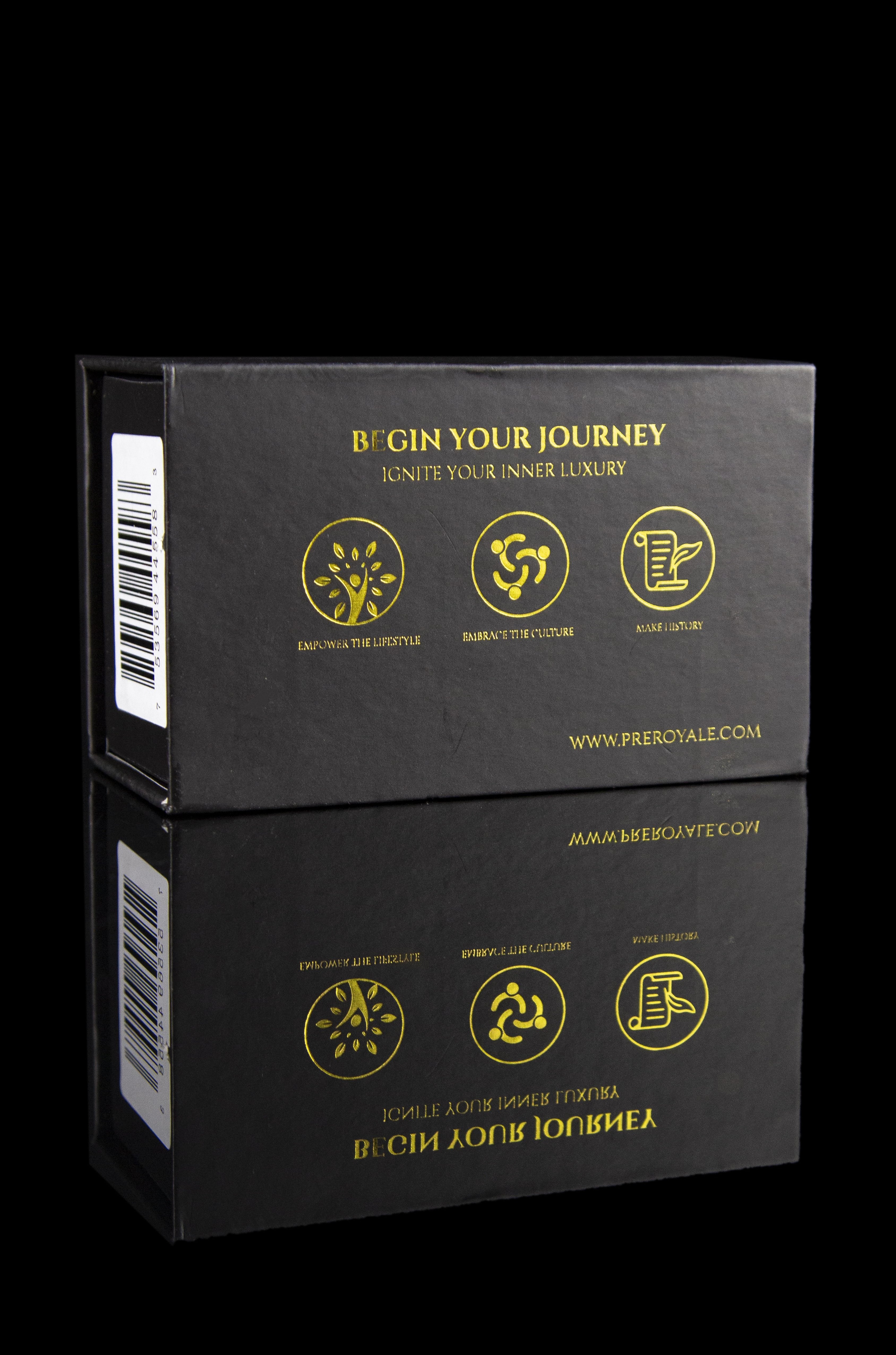 Two black boxes stacked on a dark surface, branded with gold foil text and icons promoting a cannabis lifestyle—"Begin Your Journey, Ignite Your Inner Luxury"—and a website address.