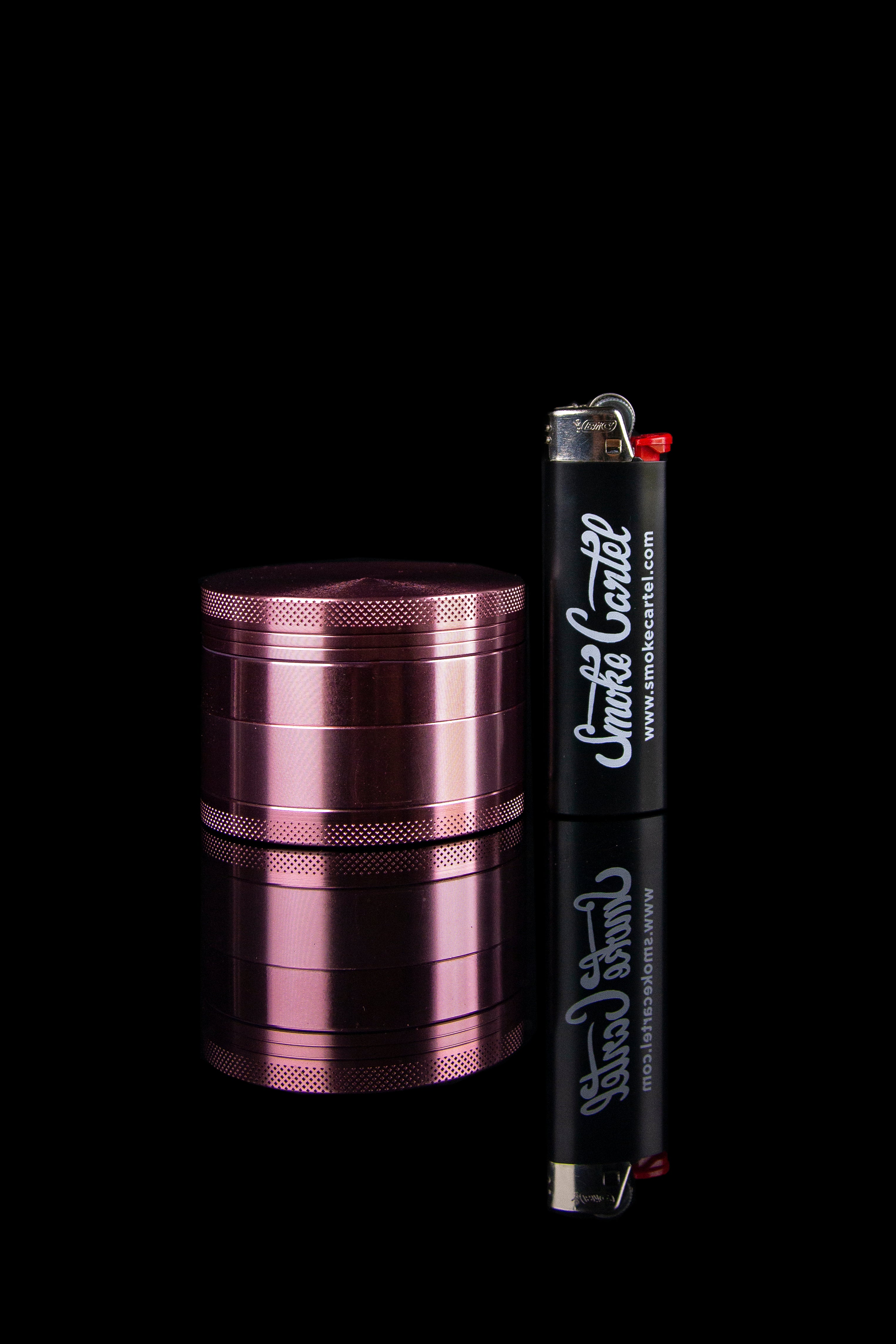 Pink metal grinder and lighter with “Smoke Cartel” branding on a black background.