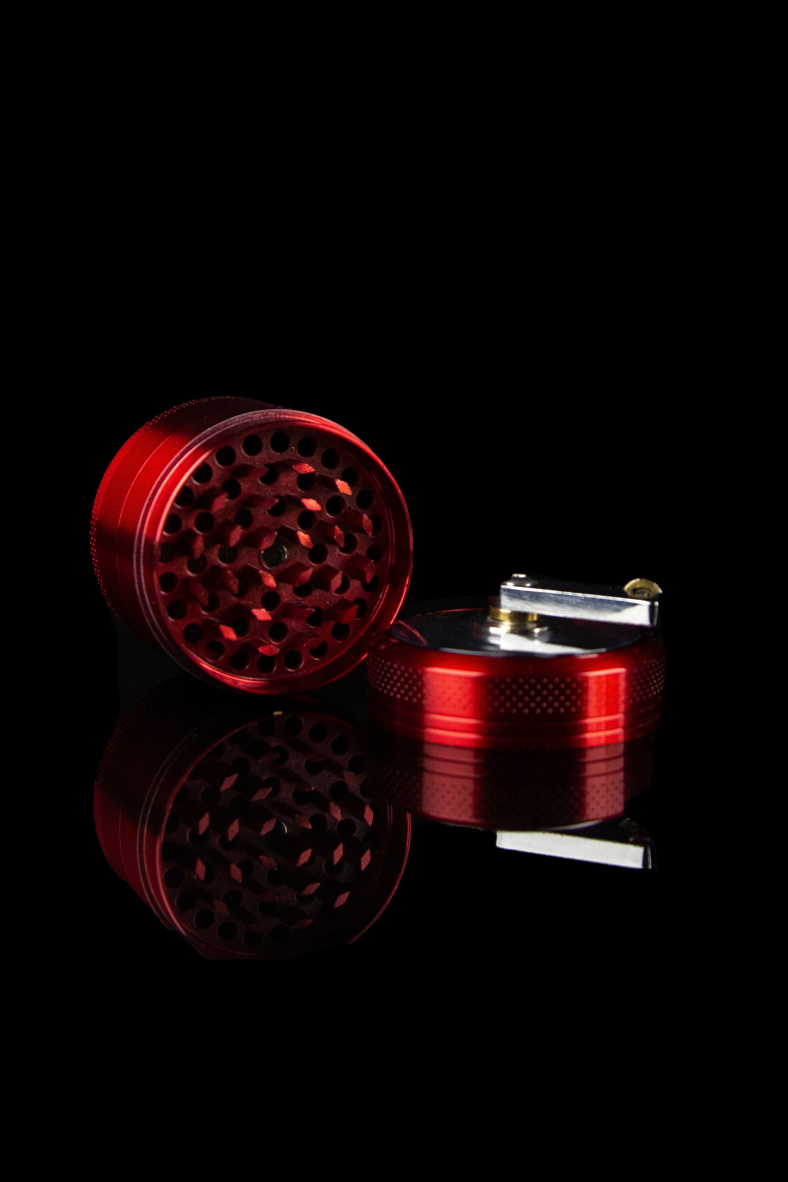 Red grinder and torch lighter on a black reflective surface.