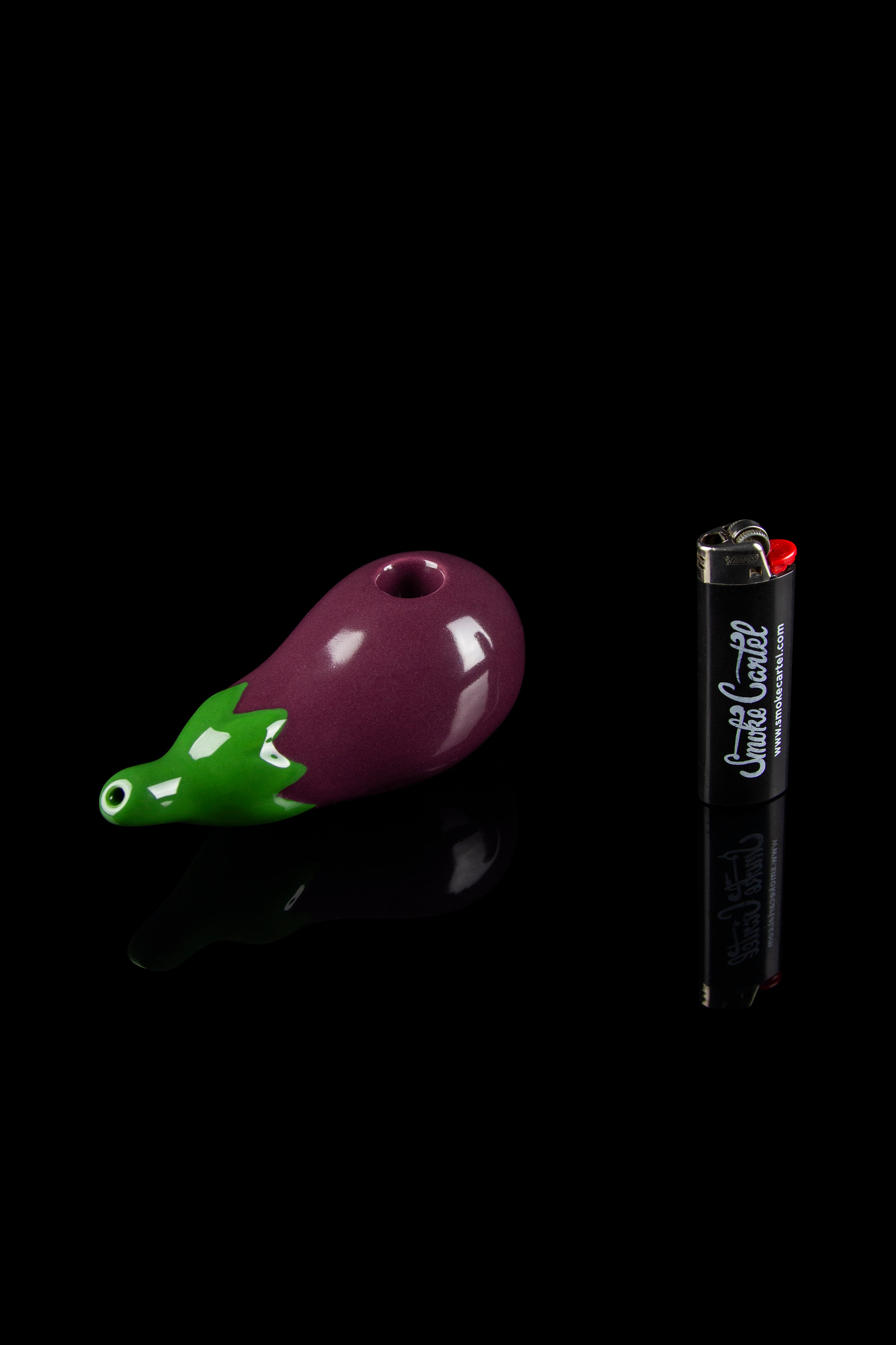 Purple glass pipe shaped like an eggplant with a green leafy stem, next to a black lighter.