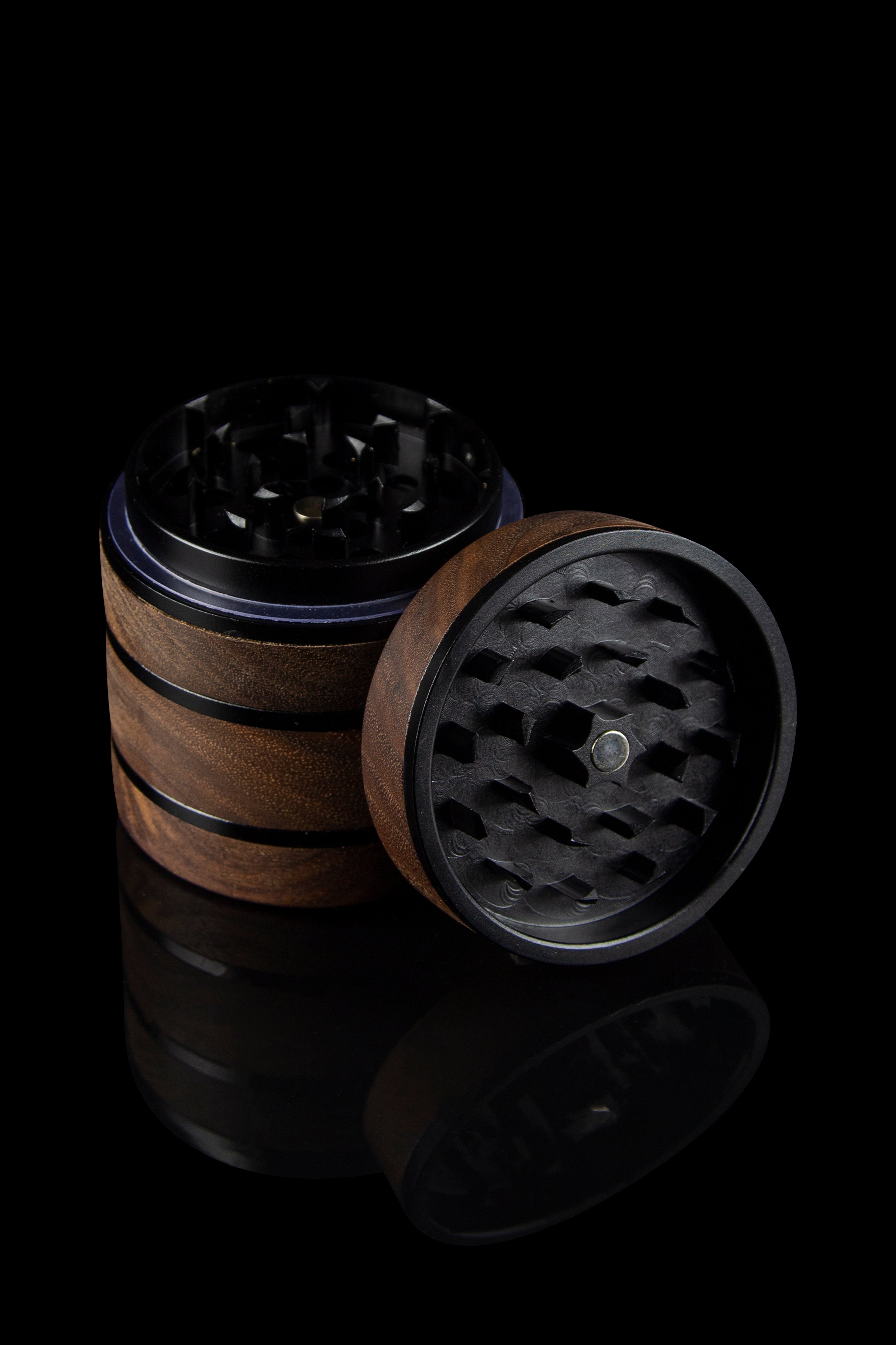 Open cannabis grinder with wooden and metal components, displayed against a dark, reflective background.