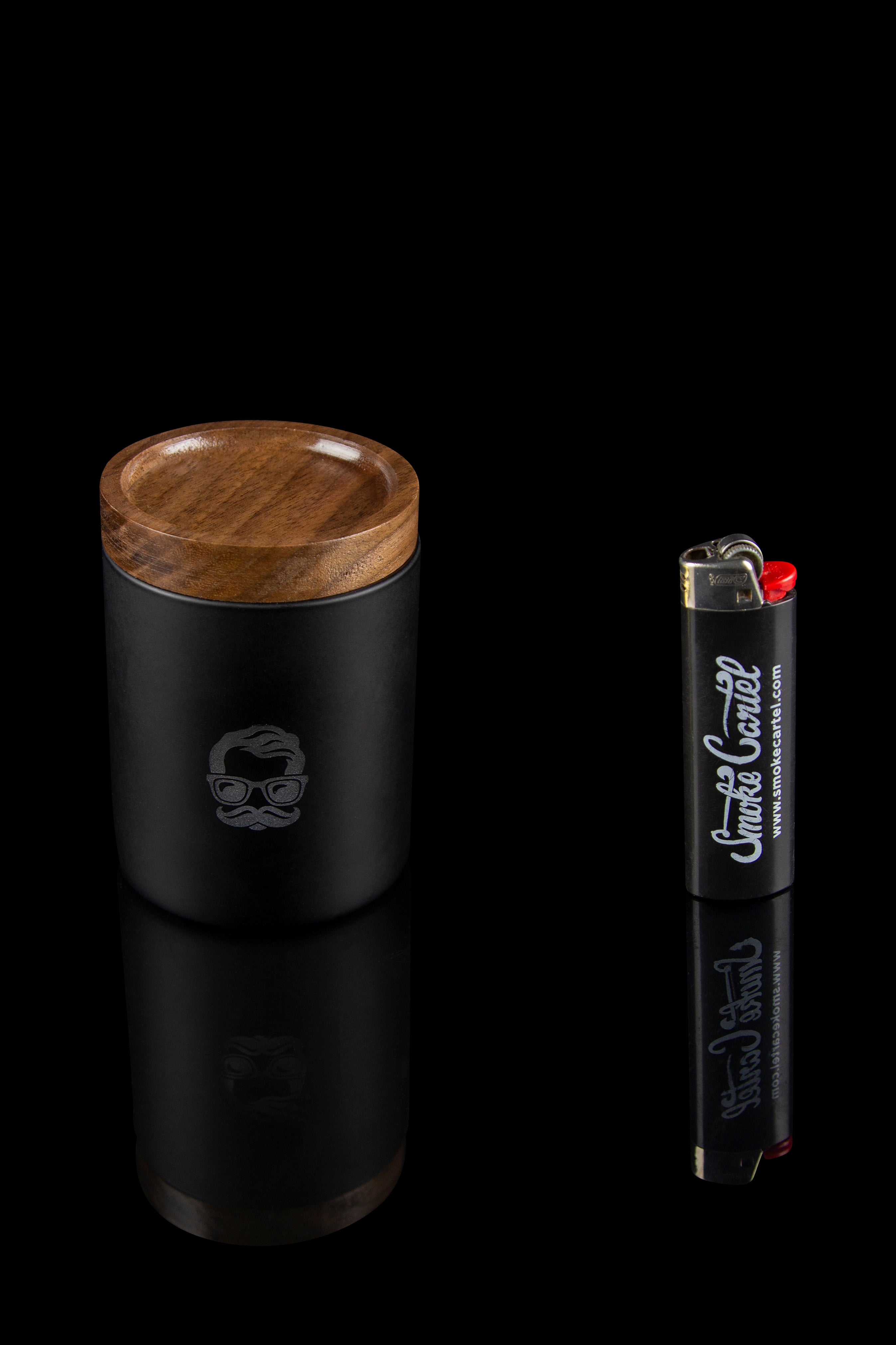 Black metal cannabis grinder with a wooden top and a branded lighter beside it.