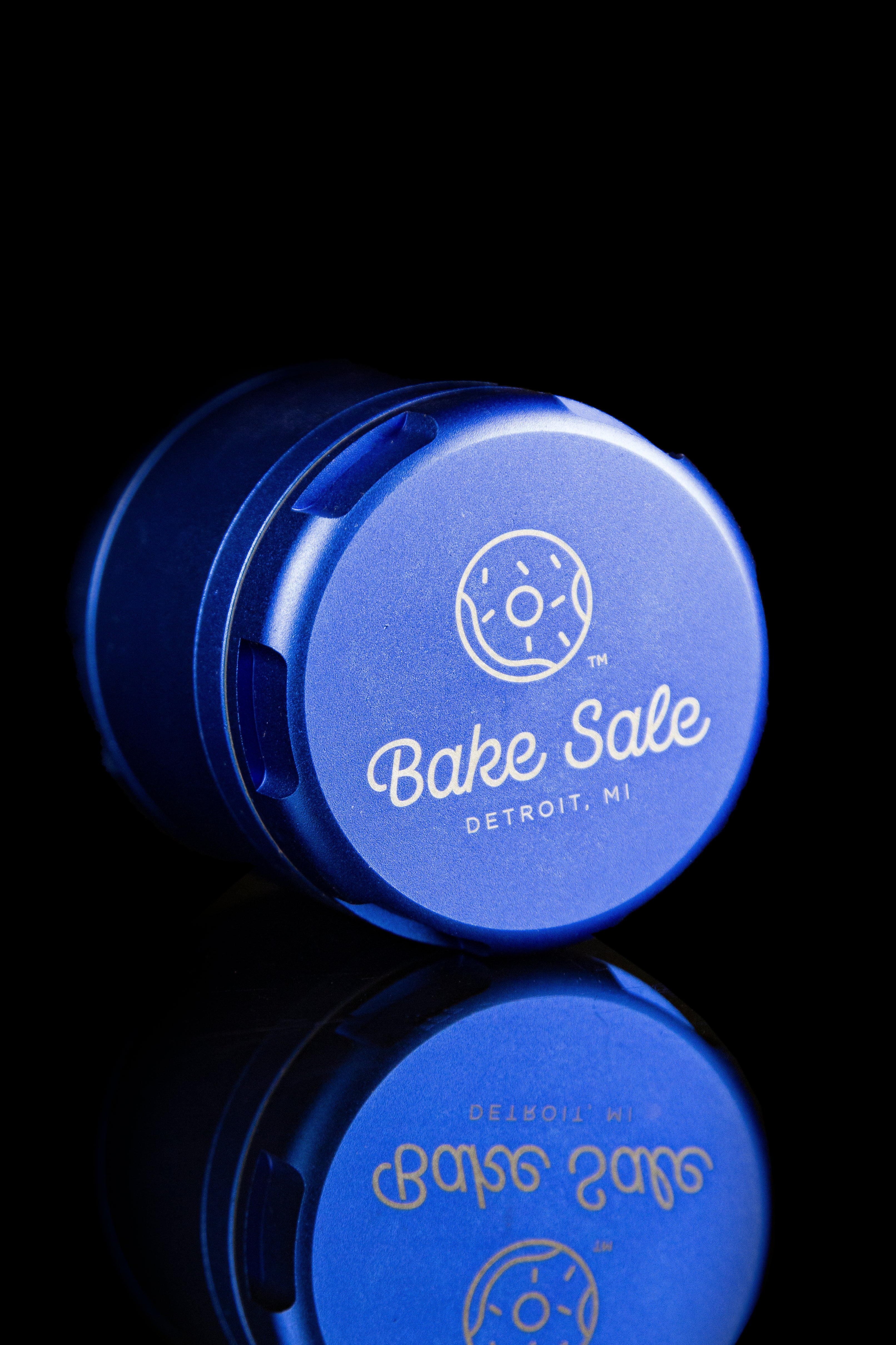 Blue cannabis container with “Bake Sale Detroit, MI” logo and mirrored reflection.