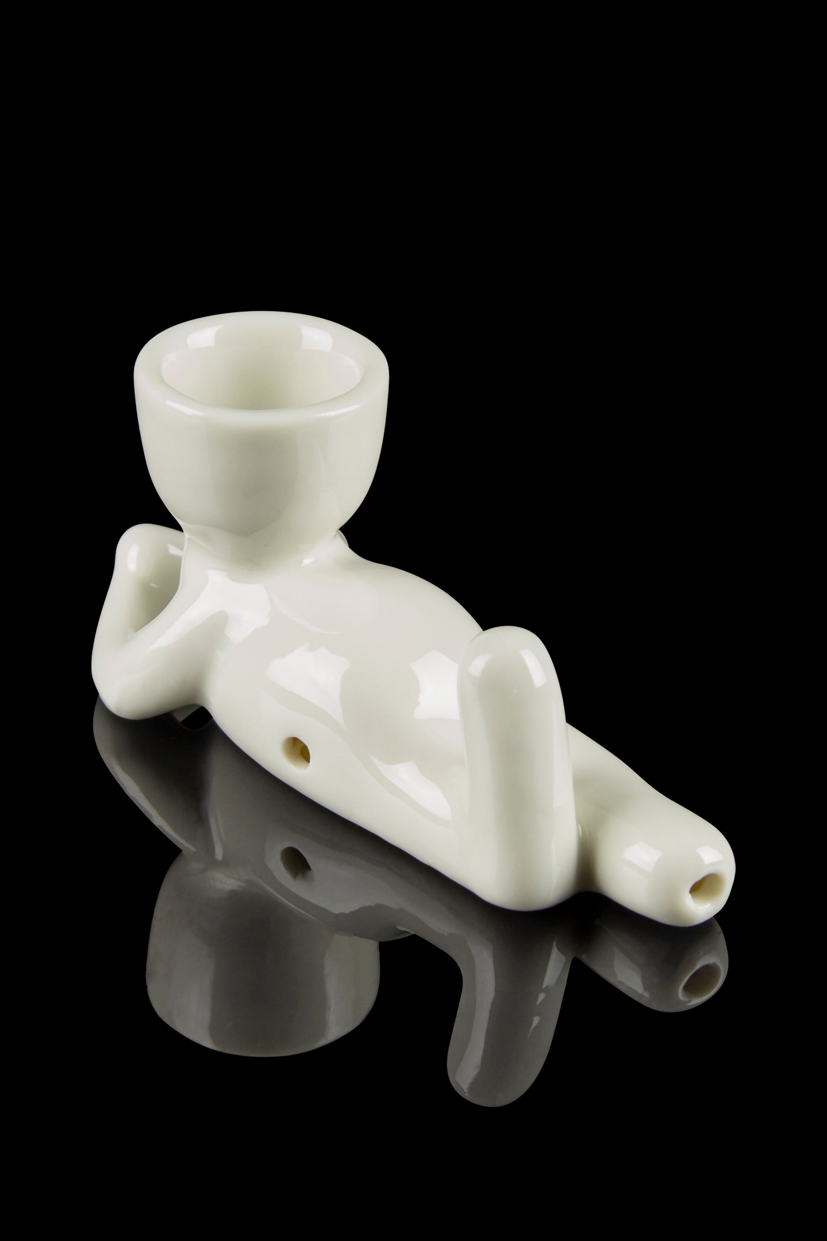 White ceramic chillum pipe shaped like a reclining figure, reflecting on a dark surface.