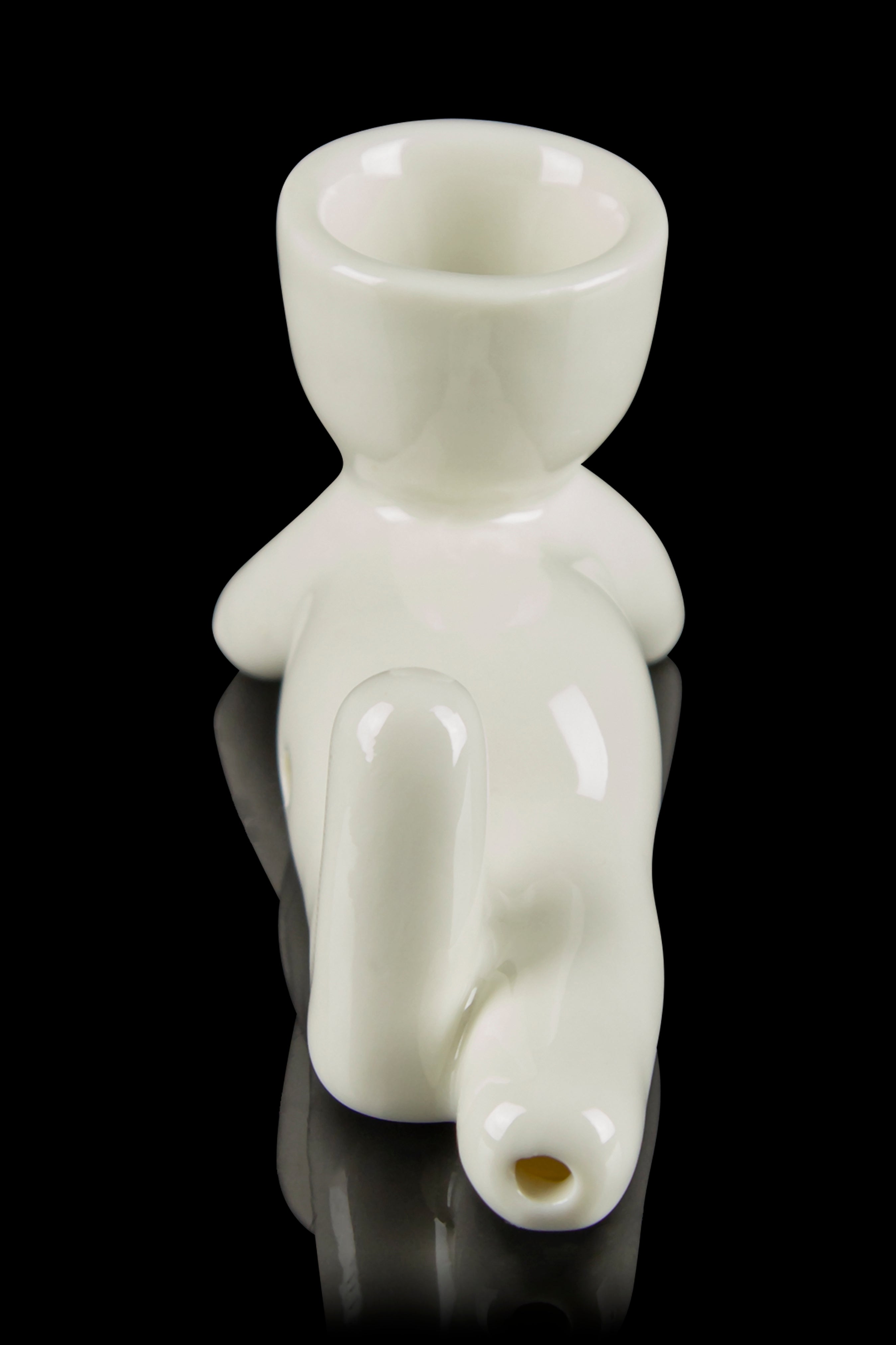 Glass bubbler shaped like a figurine with a mouthpiece and water chamber, reflecting on a black surface.
