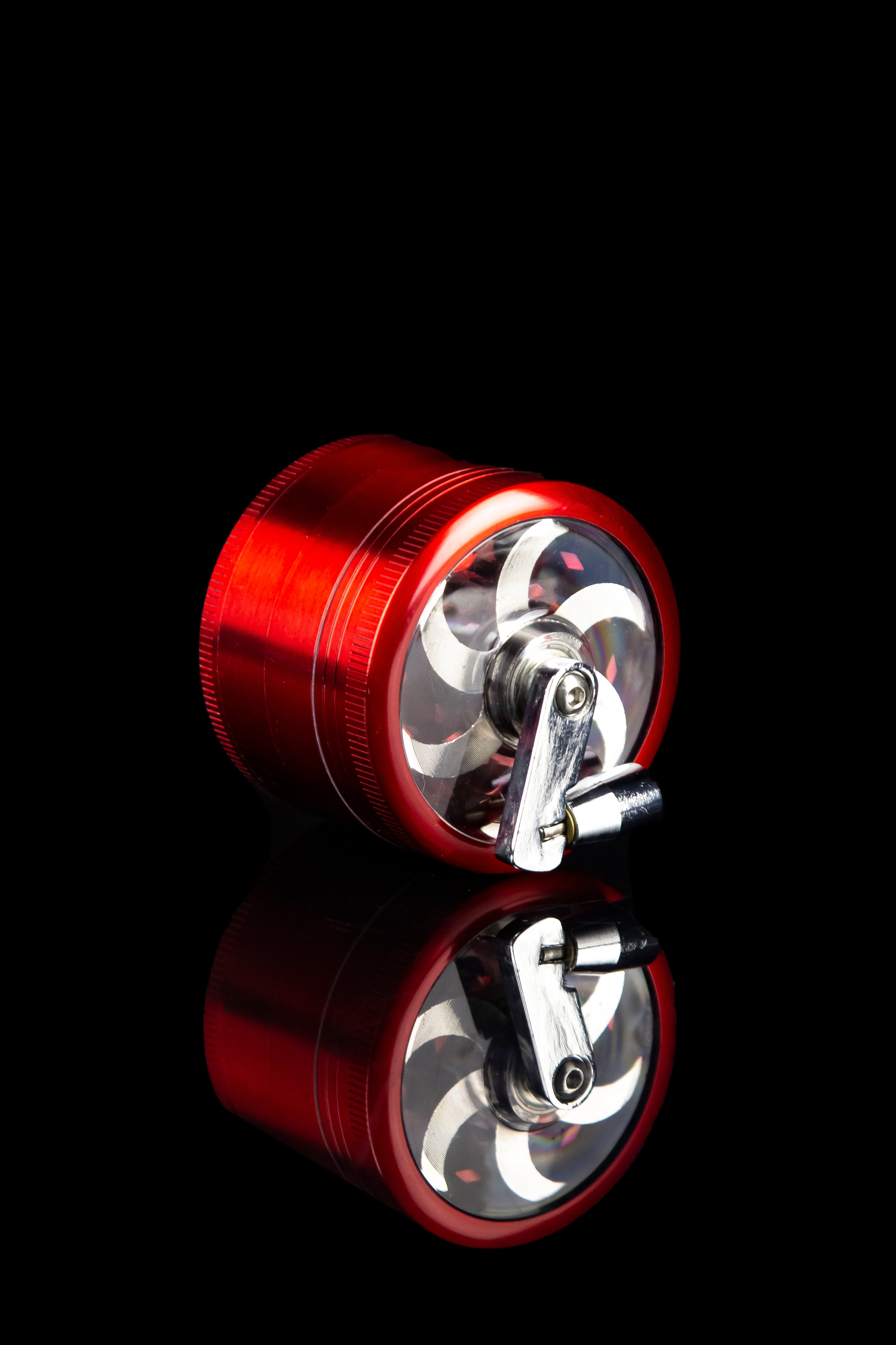 Red metal cannabis grinder with a mirrored reflection on a black surface.