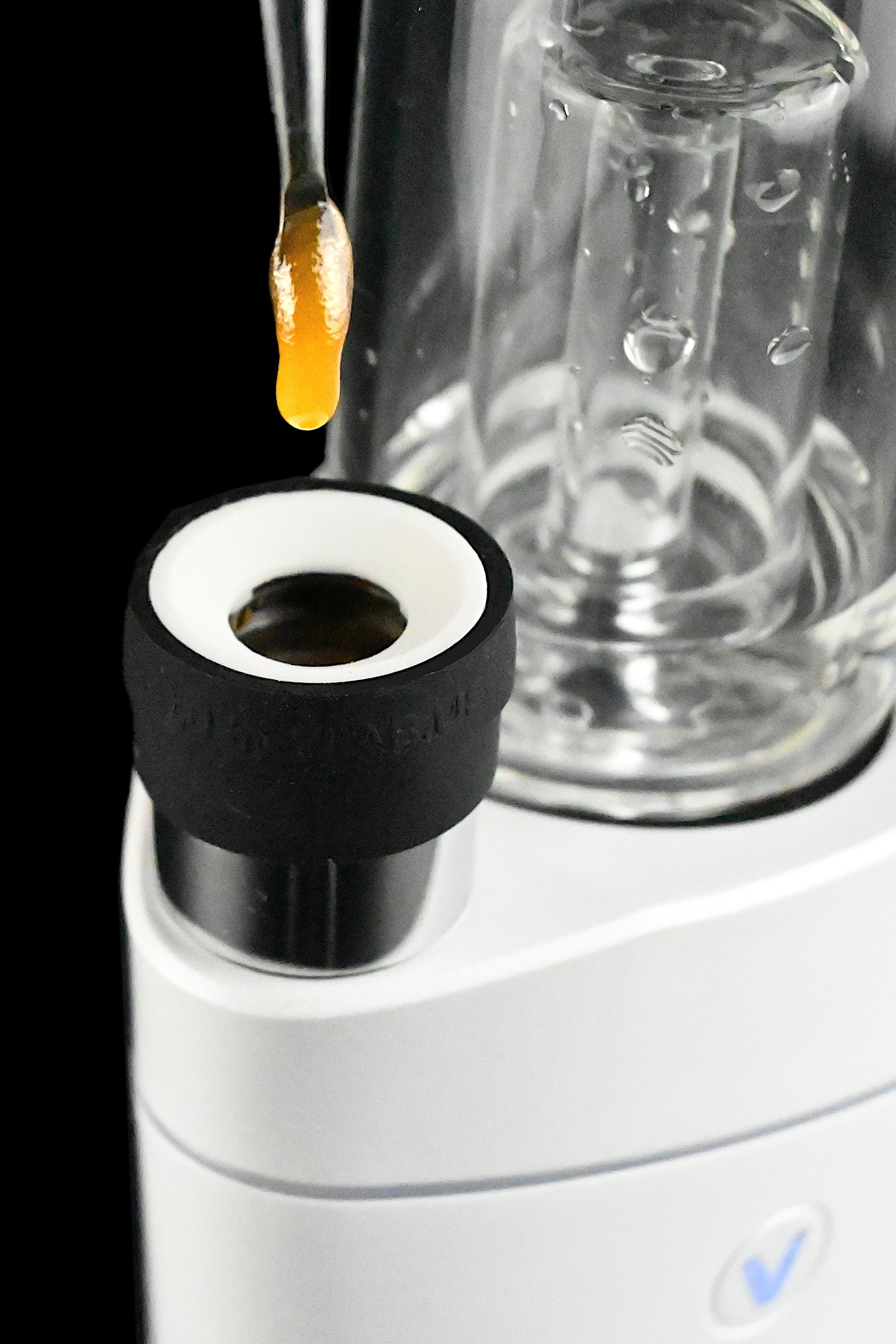 Cannabis concentrate dripping onto a vaporizer heating element with a glass bubbler in the background.