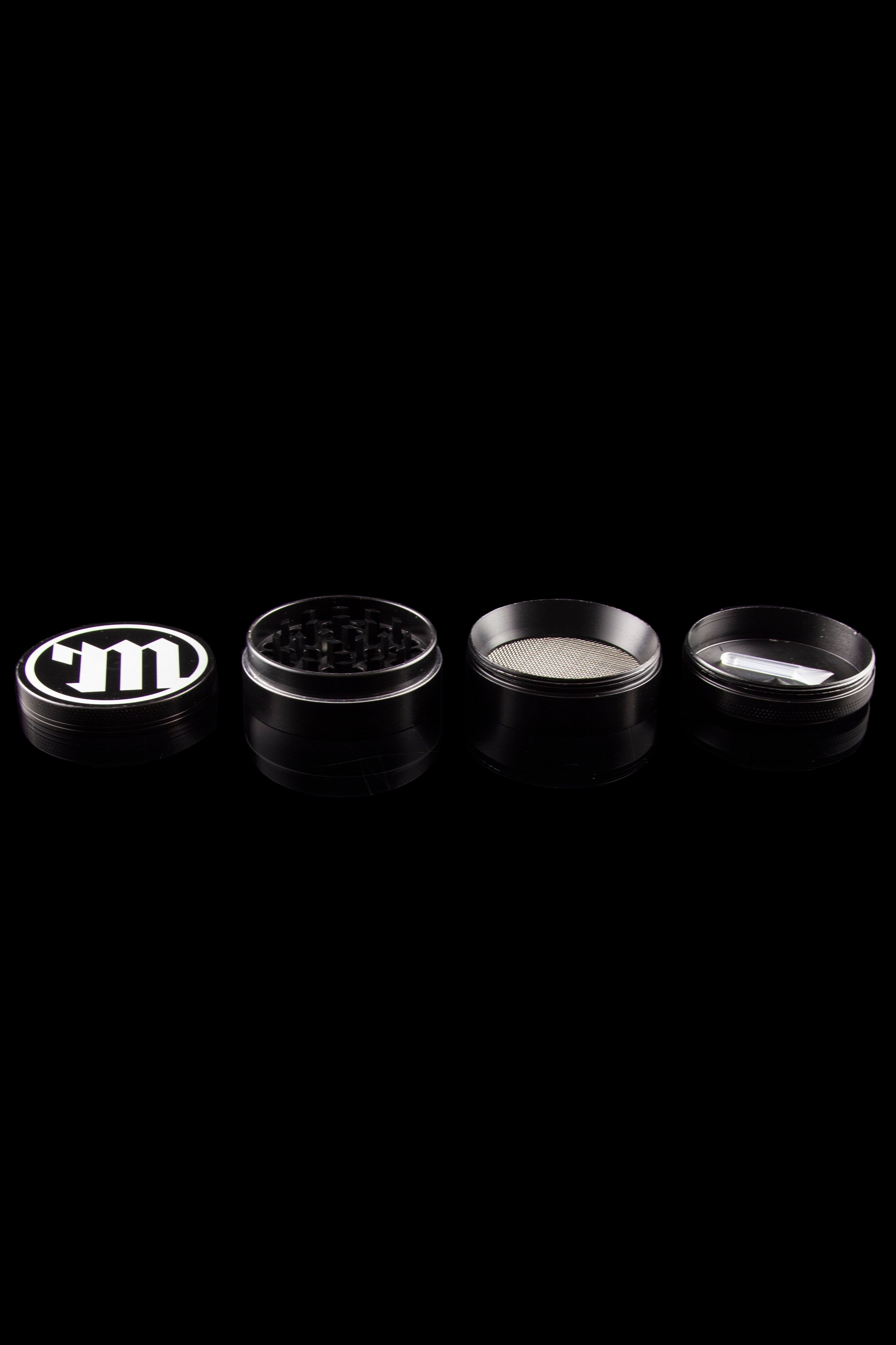 Silver cannabis grinder disassembled into its component parts on a black background.