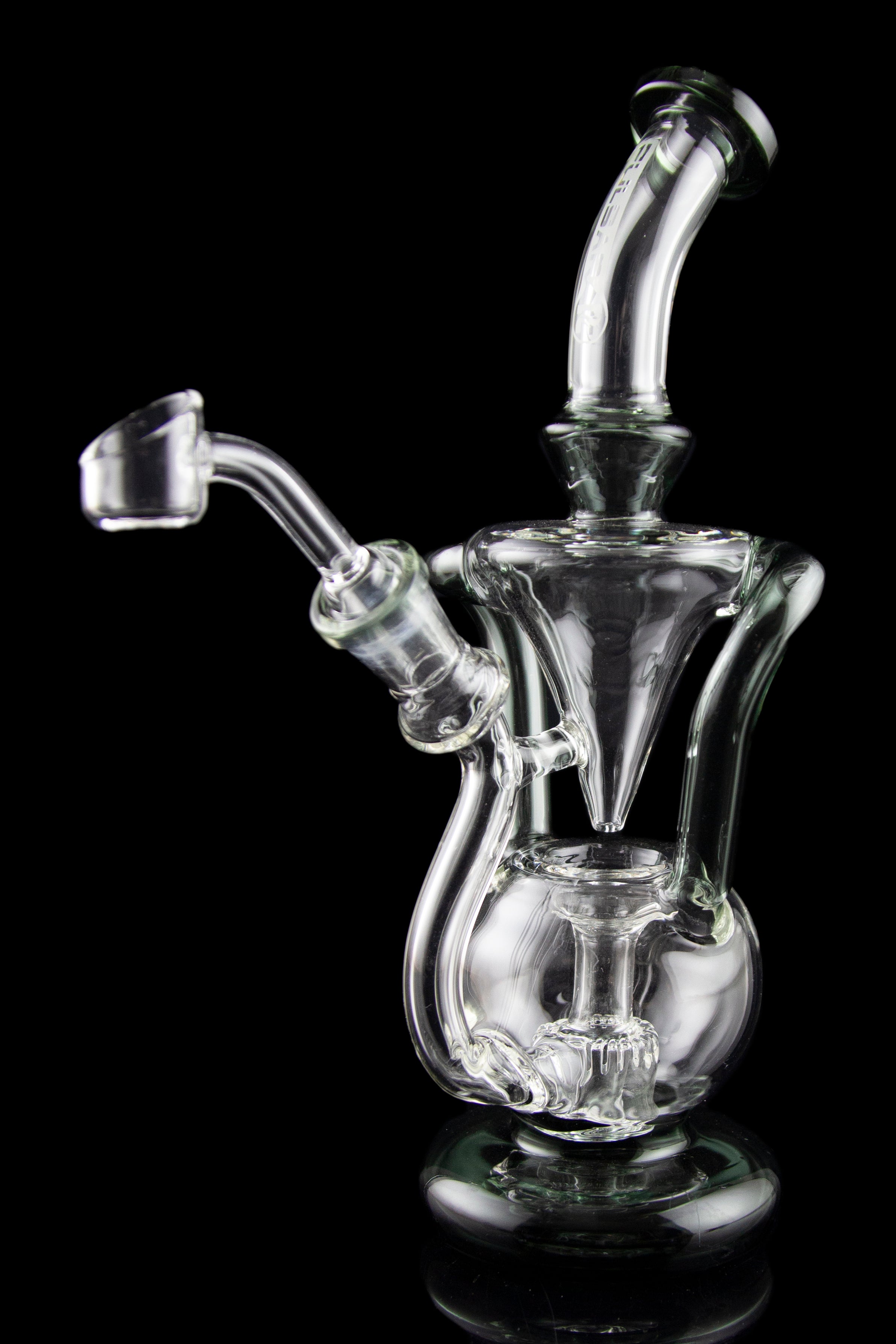 Clear glass water pipe (rig) with intricate bubbler design and a separate quartz nail for concentrates, displayed on a reflective surface against a black background.