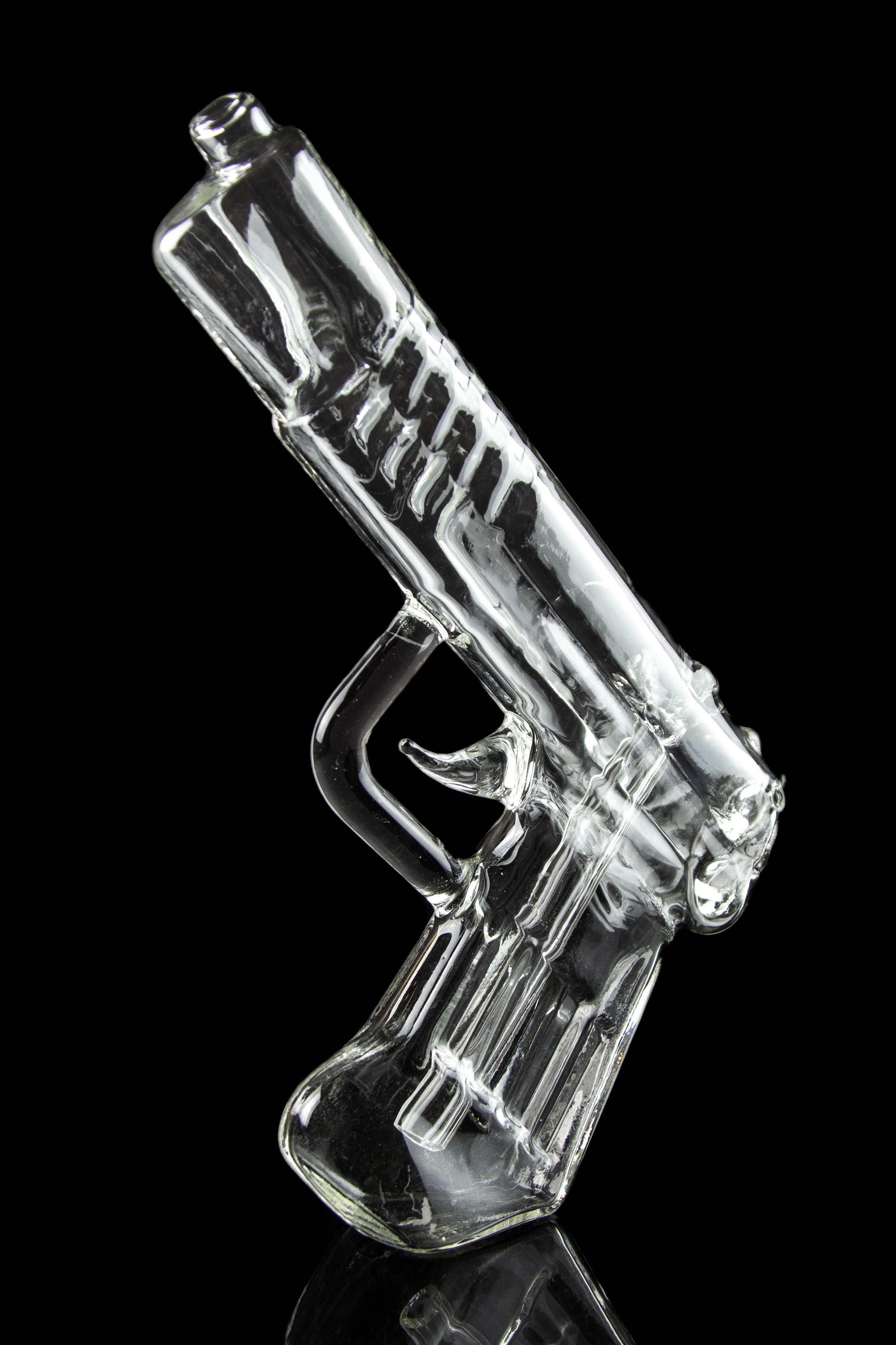 Clear glass pipe shaped like a handgun, reflecting on a black surface.