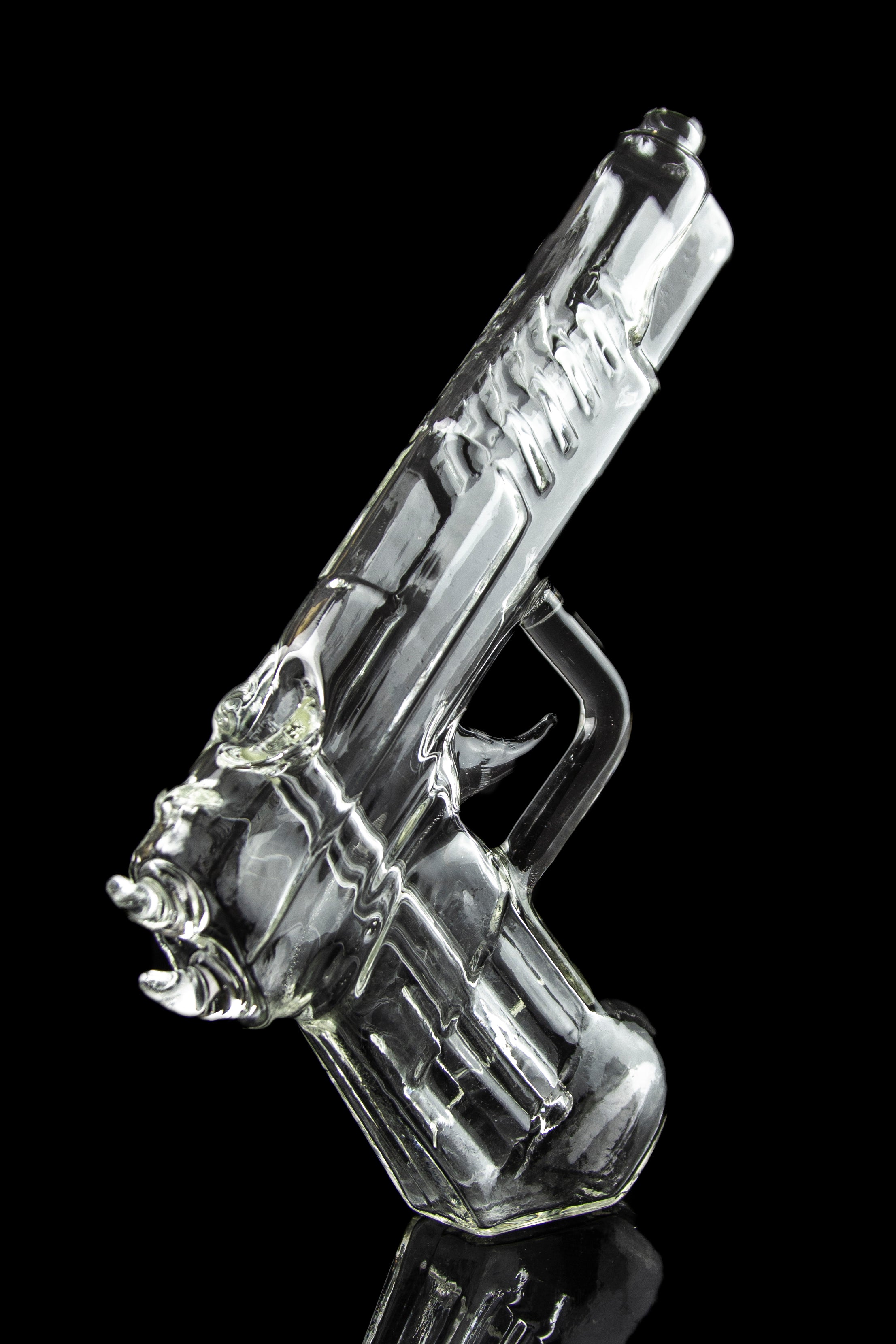 Clear glass pipe shaped like a handgun, reflecting on a black surface.
