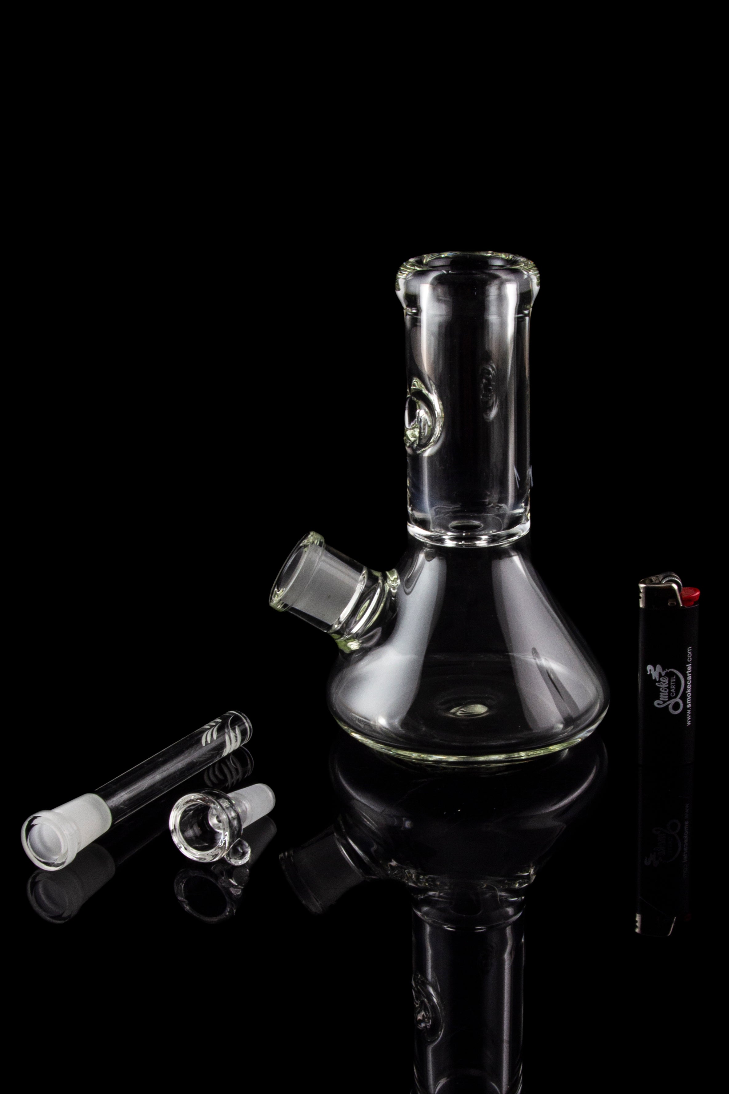 Glass bong with accessories on a black reflective surface.