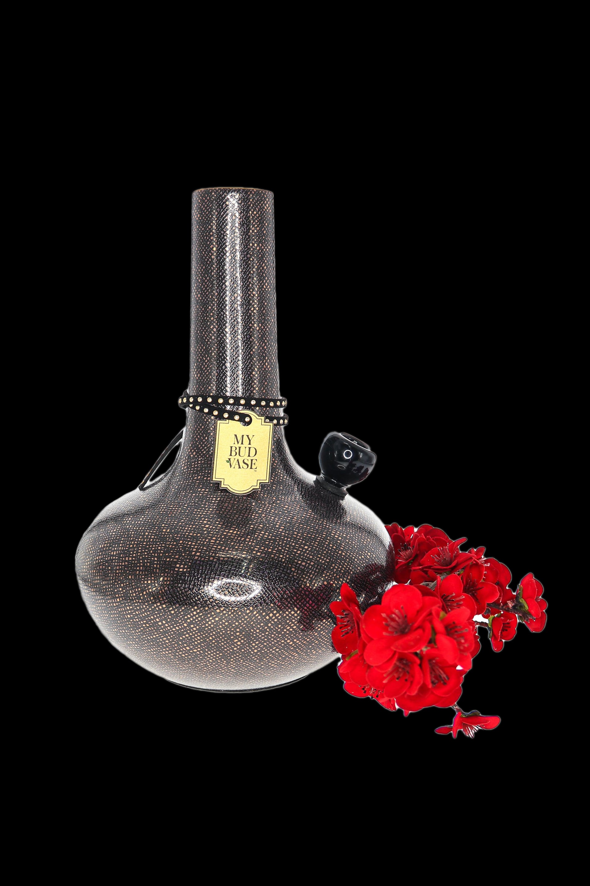 Black glass cannabis water pipe with red flowers beside it on a dark background.