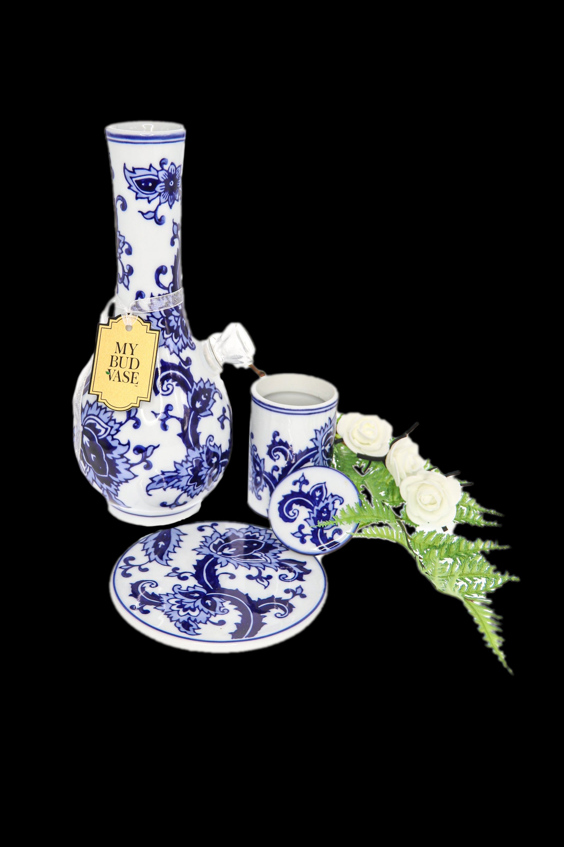 Ornate porcelain cannabis water pipe and accessories with white roses on a black background.