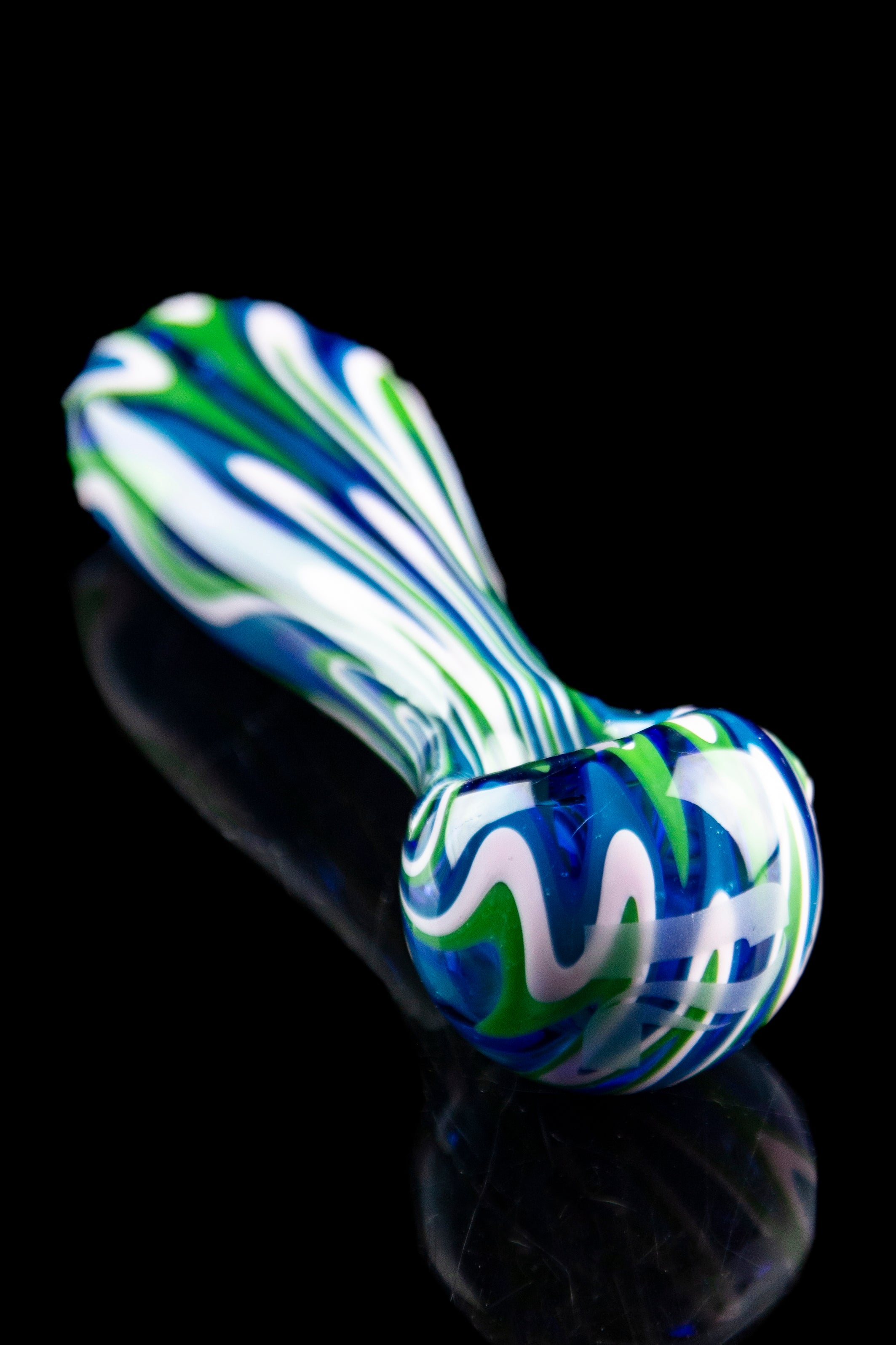 Hand-blown glass pipe with swirling blue, green, and white patterns, reflecting on a dark surface.
