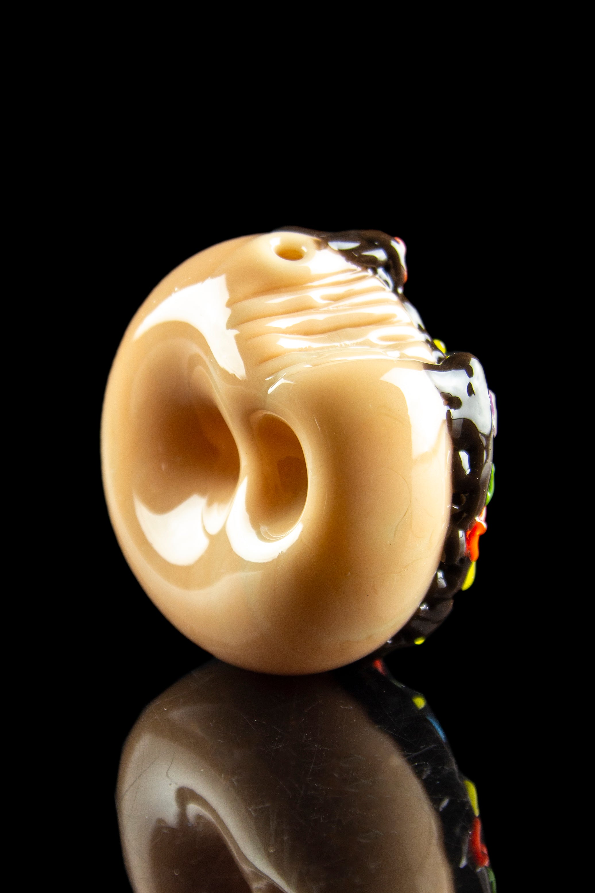 Glass skull pipe with colorful accents, reflecting on a dark surface.